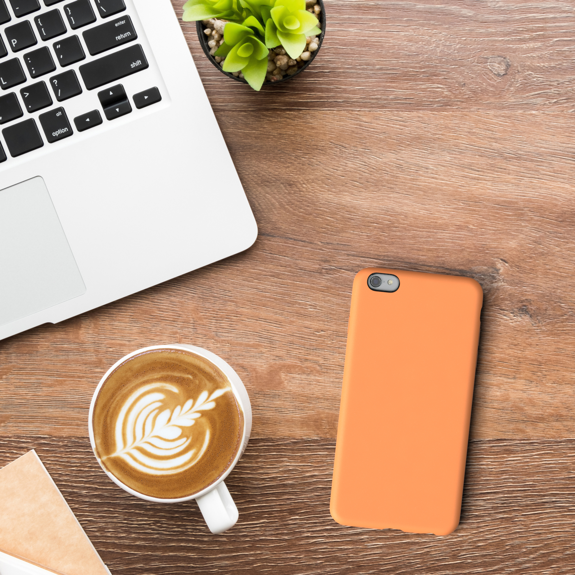 Laptop, Kaffee, orangefarbene Handyhülle und eine Pflanze auf Holz.