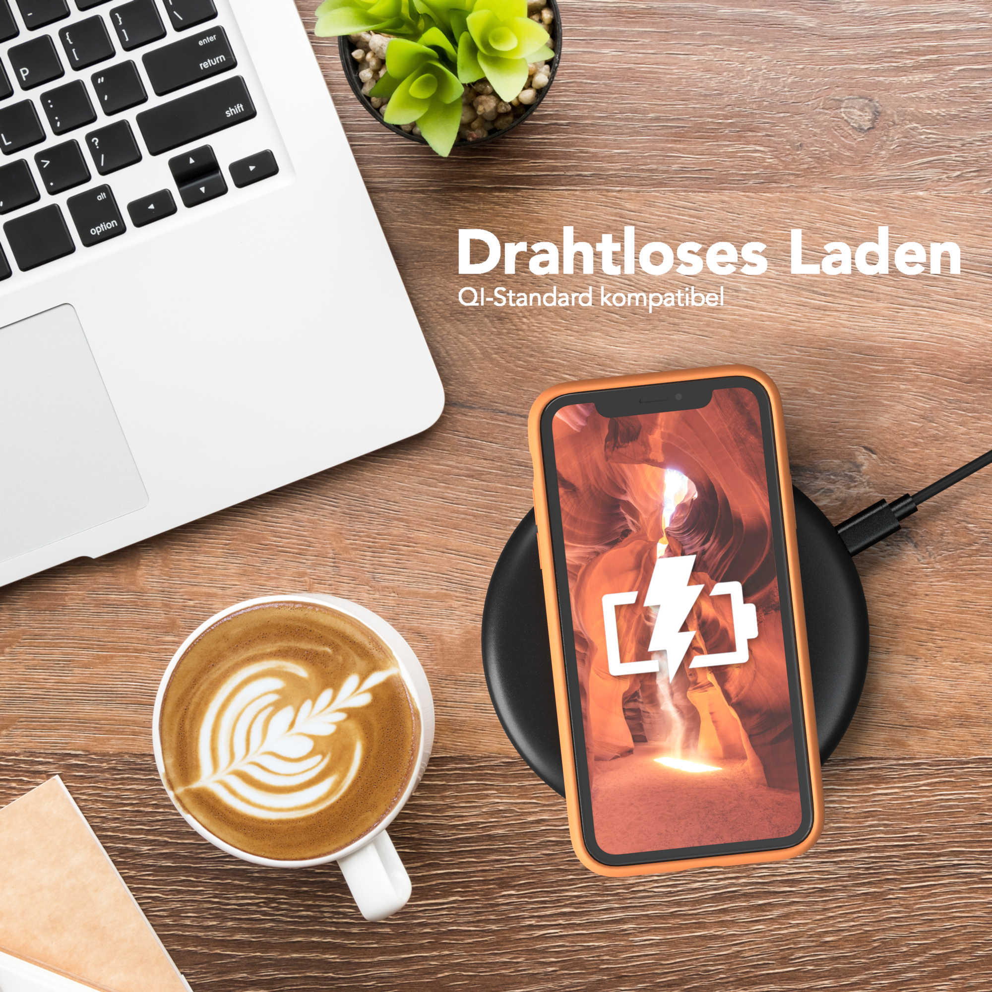 Ein Telefon auf einem kabellosen Ladegerät, ein Laptop und eine Kaffeetasse mit Latte Art auf Holz.