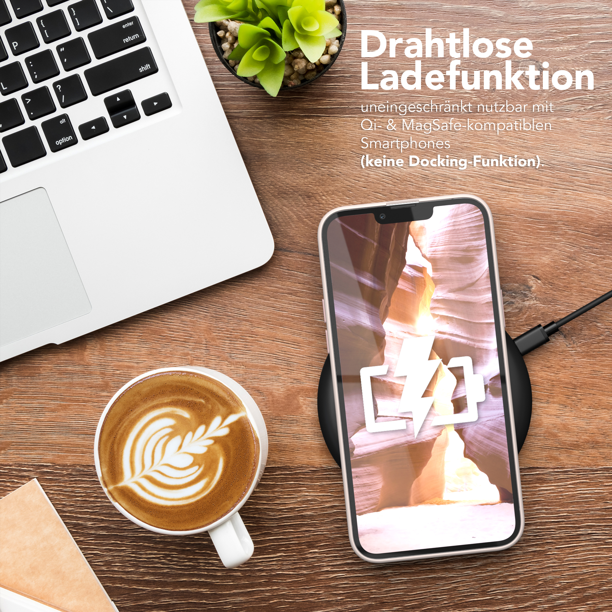 Ein Telefon, das drahtlos auf einem Pad geladen wird, neben einem Laptop und einer Kaffeetasse mit Latte Art.
