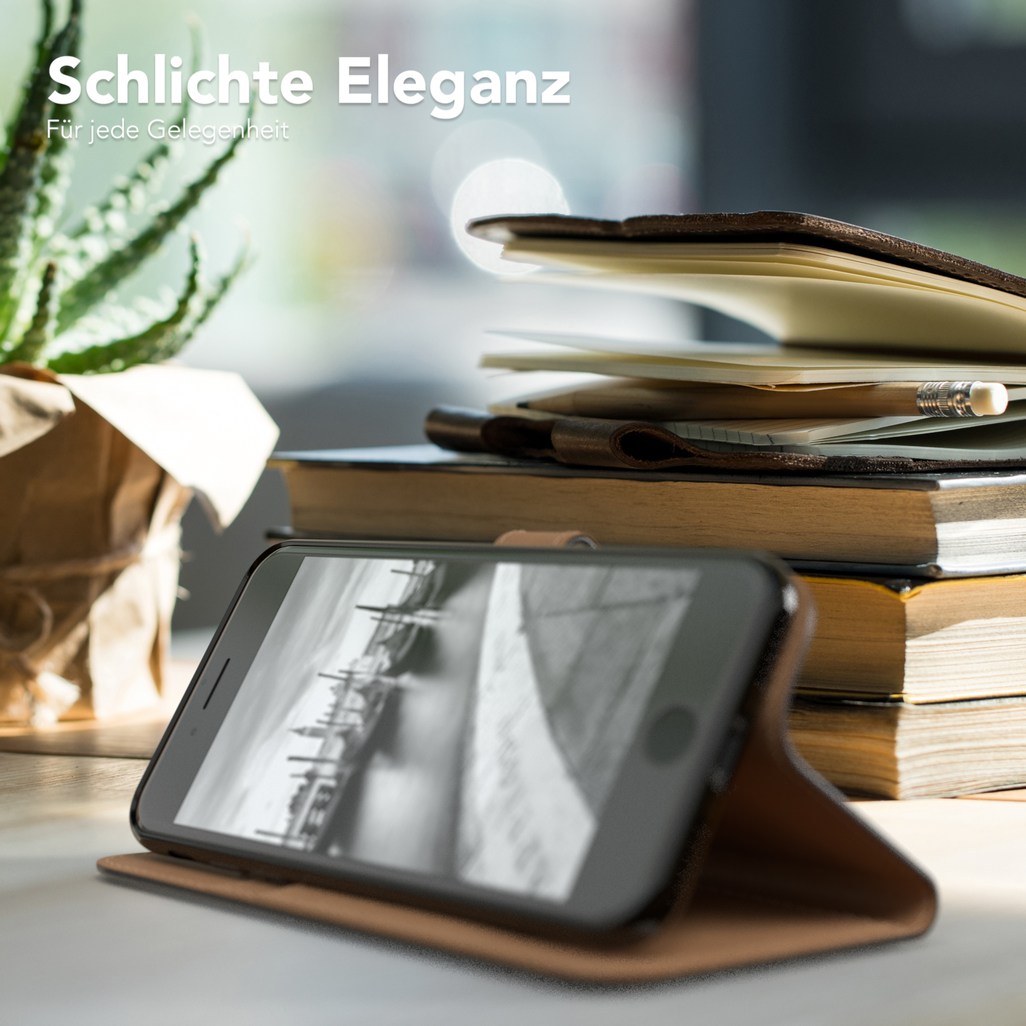 Ein Telefon in einer braunen Hülle auf einem Tisch mit Büchern und einer Pflanze. Der Bildschirm zeigt ein SW-Bild.