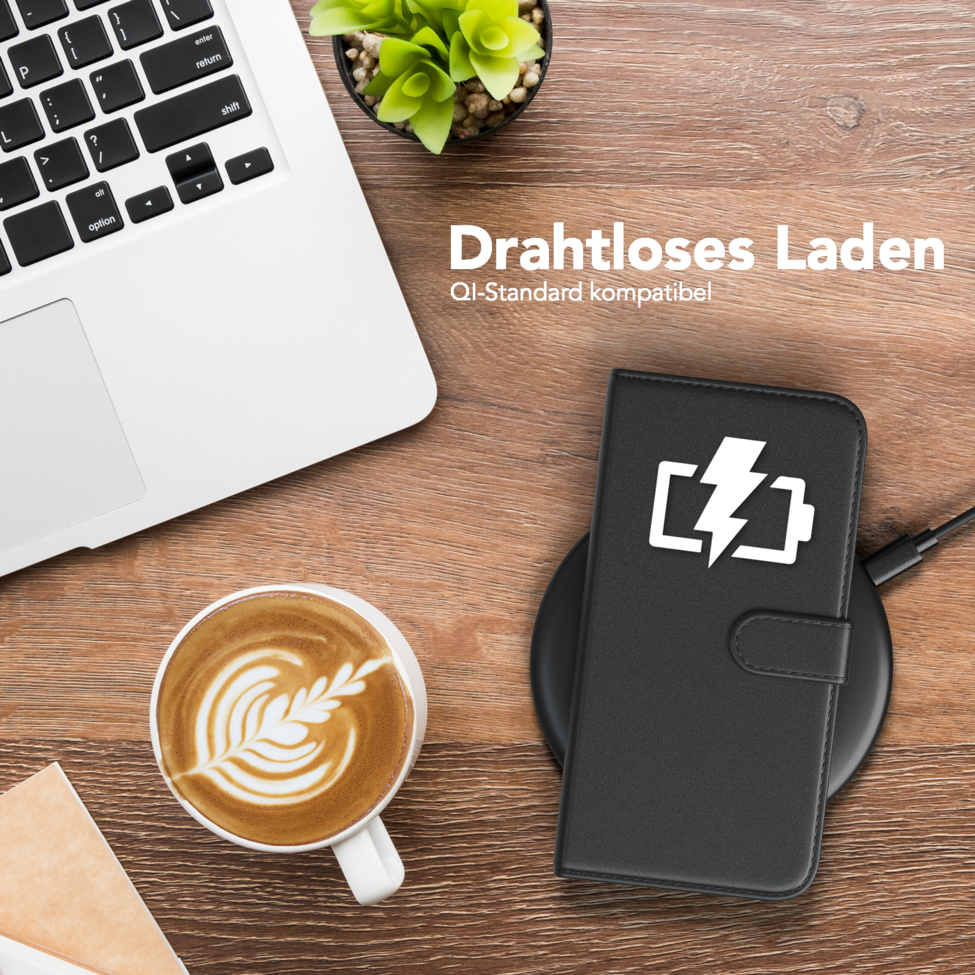 Ein Telefon wird drahtlos auf einem schwarzen Pad aufgeladen. Auf dem Holztisch befinden sich ein Laptop und eine Tasse Kaffee.