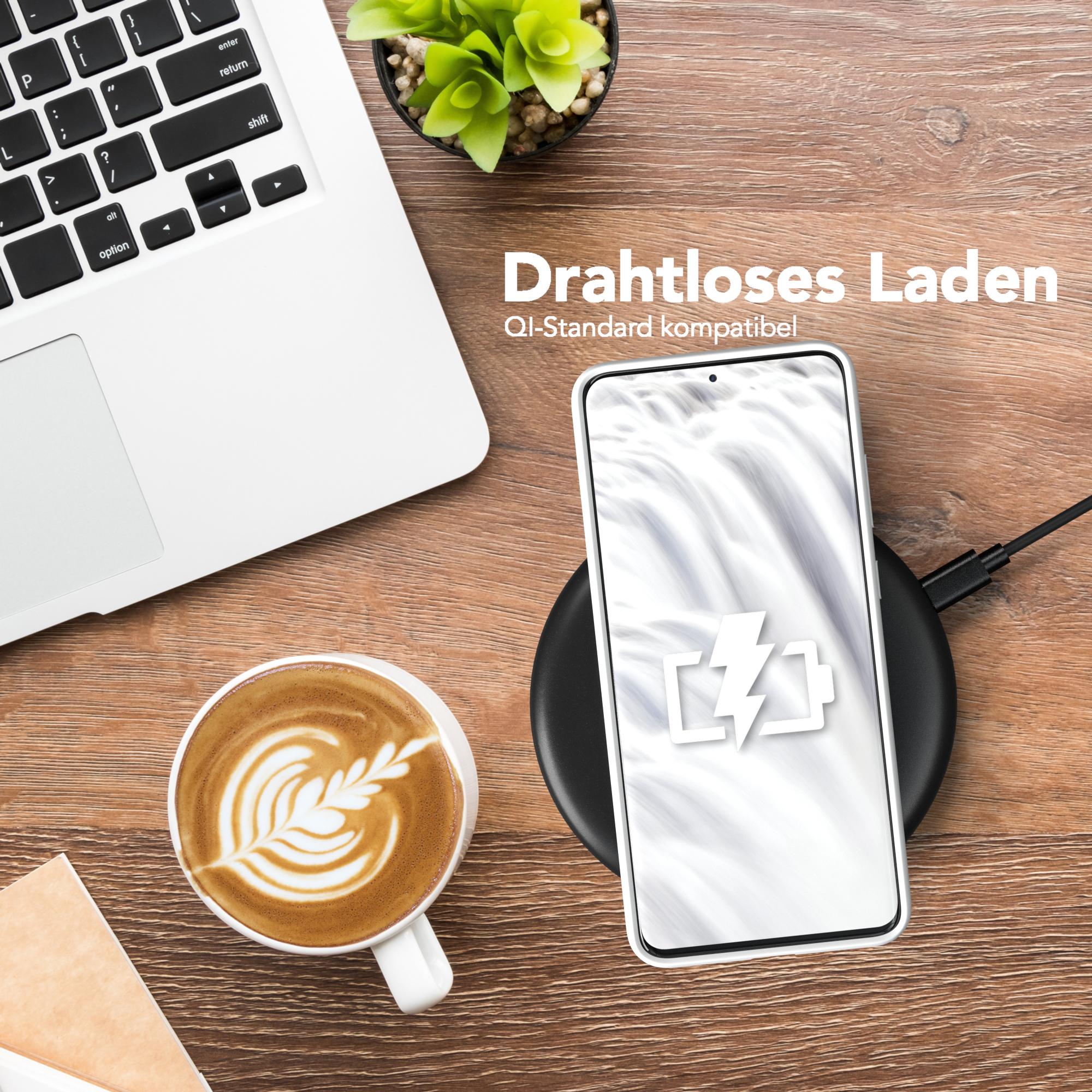 Ein Telefon wird drahtlos auf einem schwarzen Pad aufgeladen. Auf dem Holztisch befinden sich ein Laptop und eine Tasse Kaffee.