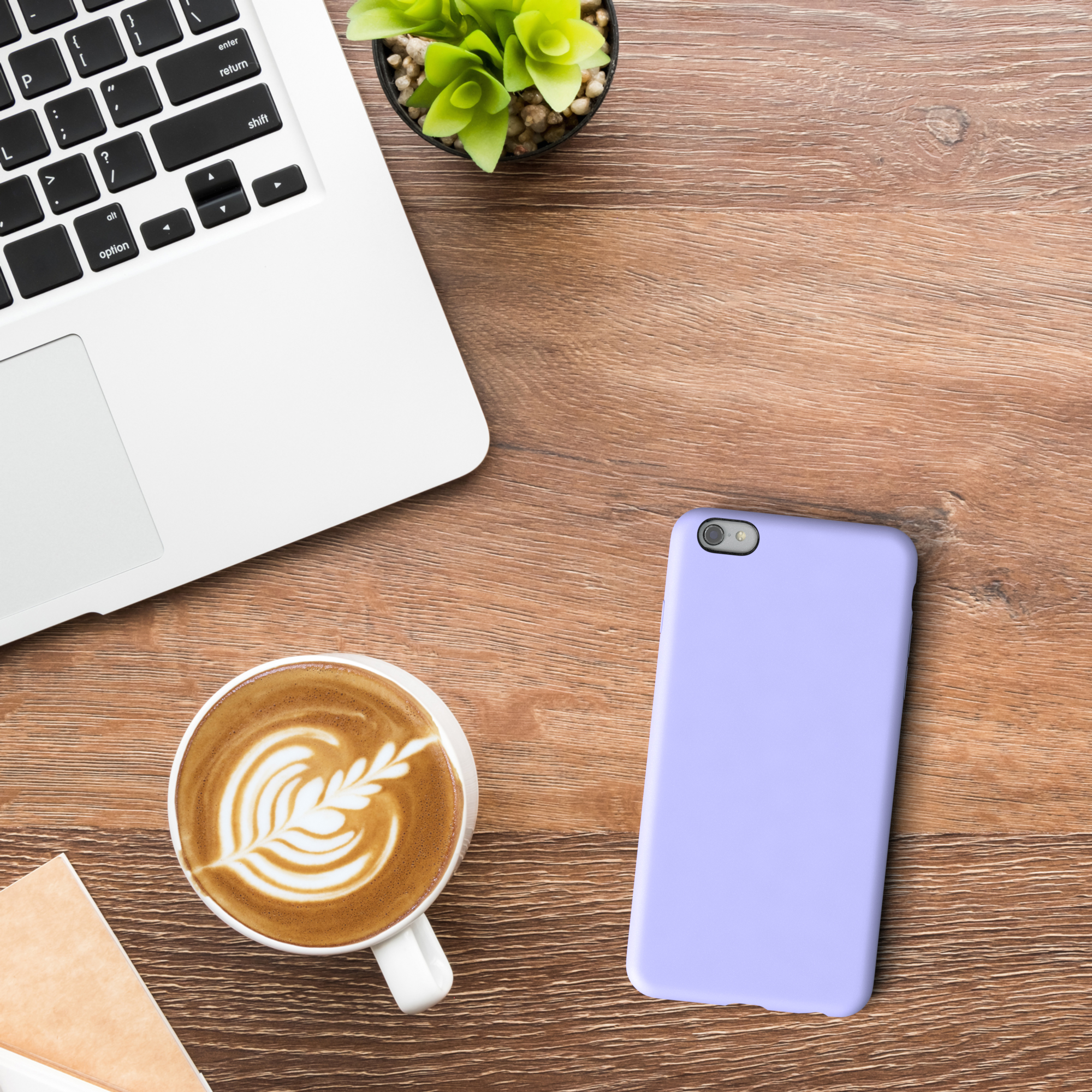 Ein Laptop, ein Telefon, eine Kaffeetasse mit Kunst und eine Pflanze auf einem Holztisch.