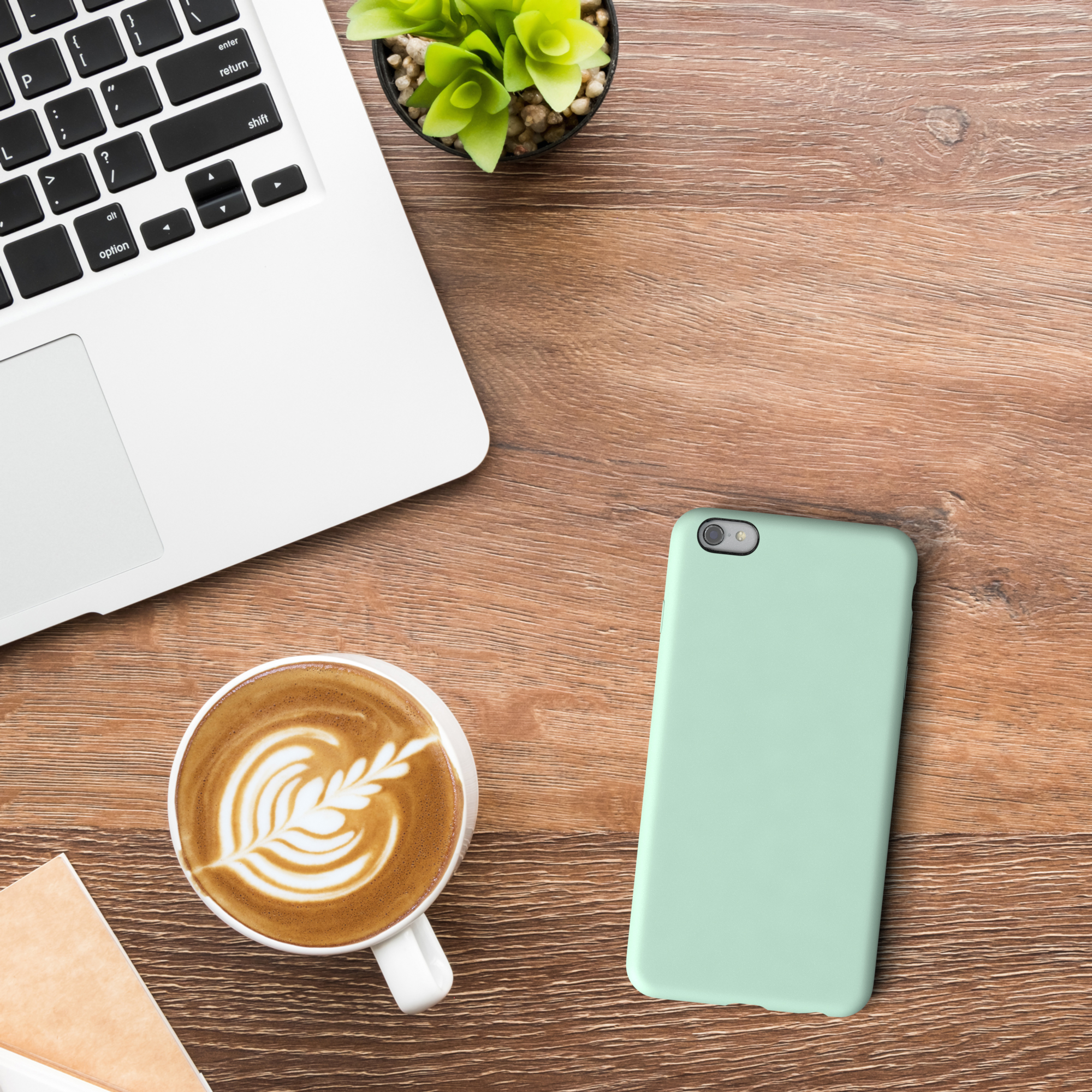 Ein Laptop, eine Kaffeetasse und eine grüne Handyhülle auf einem Holztisch. Draufsicht.