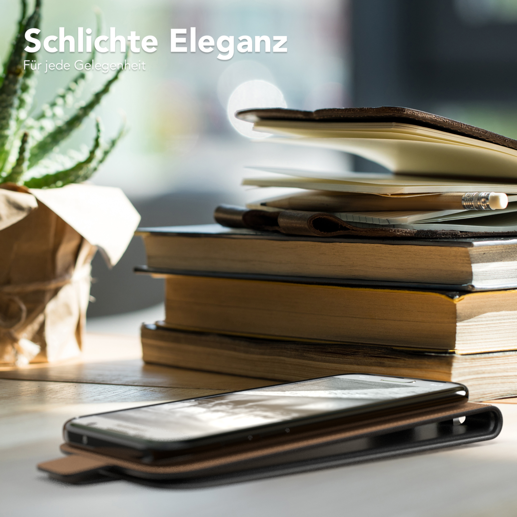 Smartphone in einer braunen Lederhülle, neben Büchern und einer Pflanze auf einem Tisch.