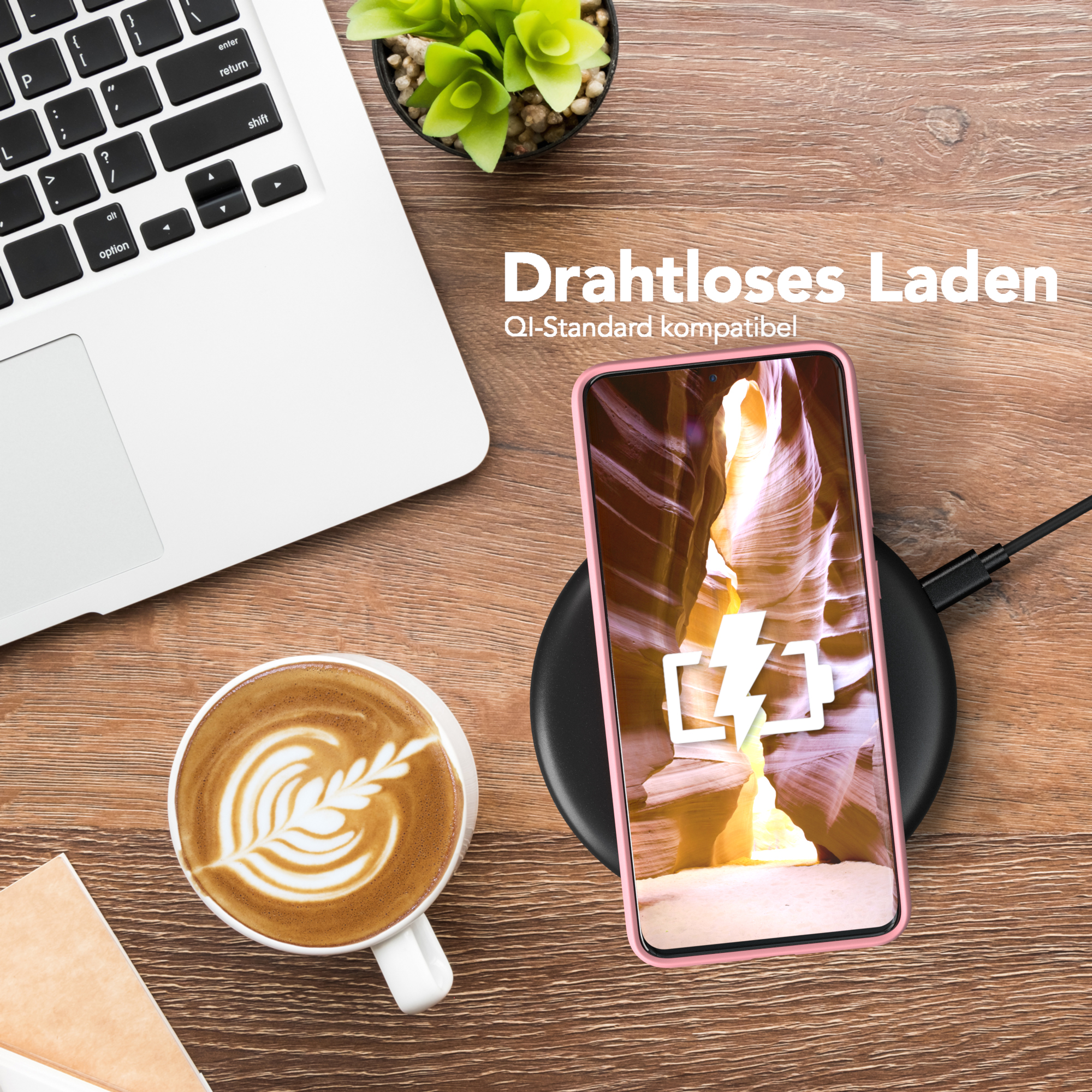 Rosa Telefon wird drahtlos auf einem Ständer geladen, neben einem Laptop und einer Tasse Kaffee.