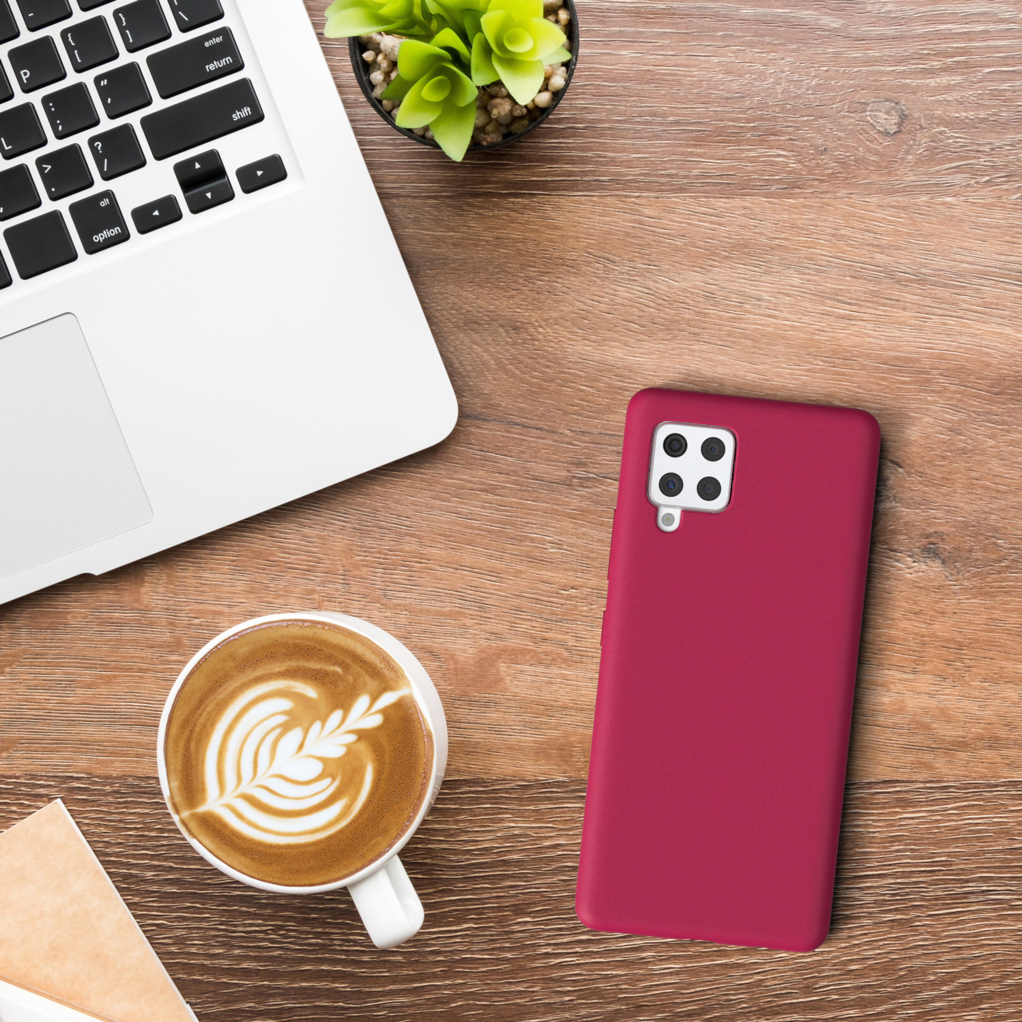 Laptop, Kaffee, Telefon auf einem Holztisch. Das Telefon befindet sich in einer roten Hülle.