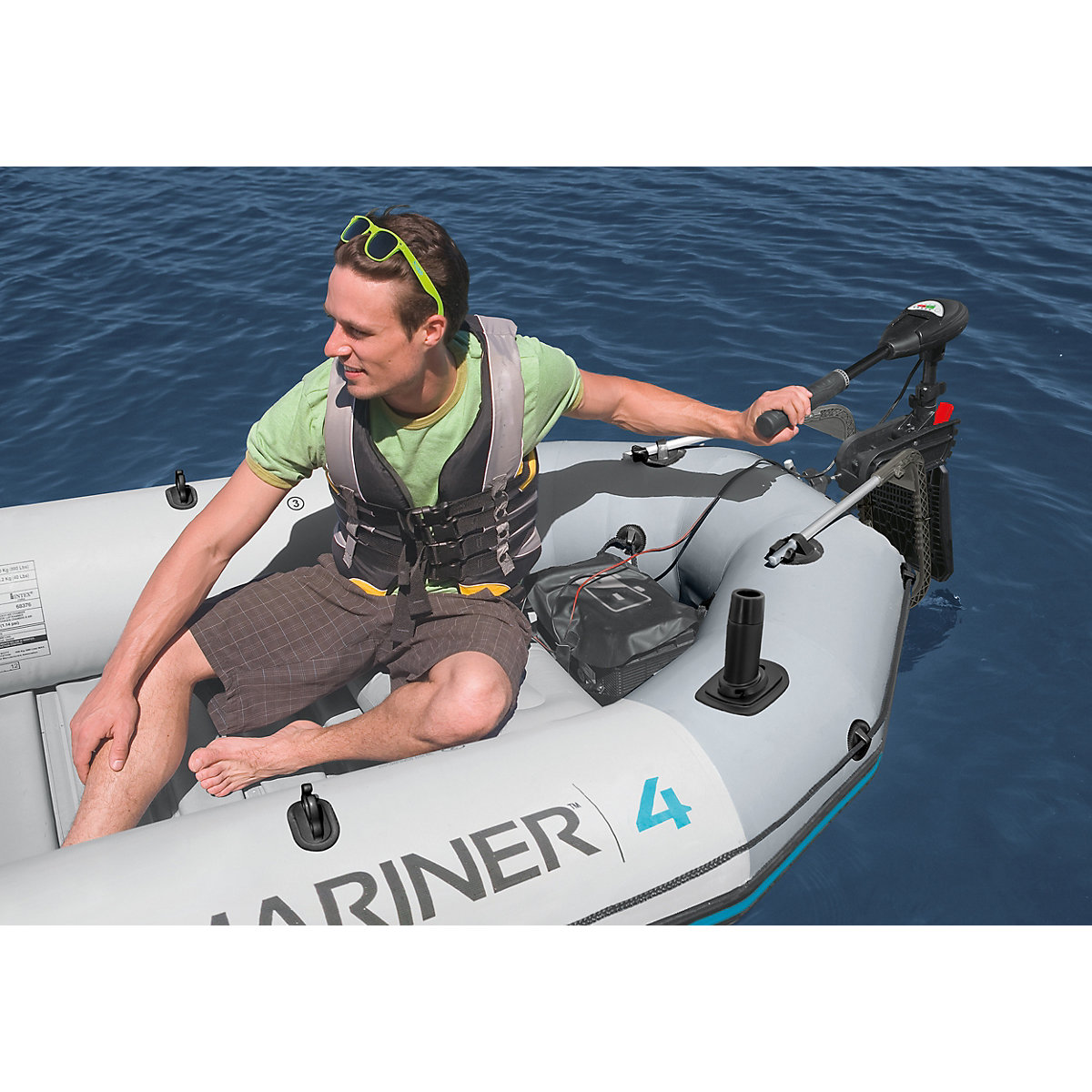 Ein Mann in einer Schwimmweste bedient einen kleinen Motor auf einem grauen Schlauchboot auf blauem Wasser.