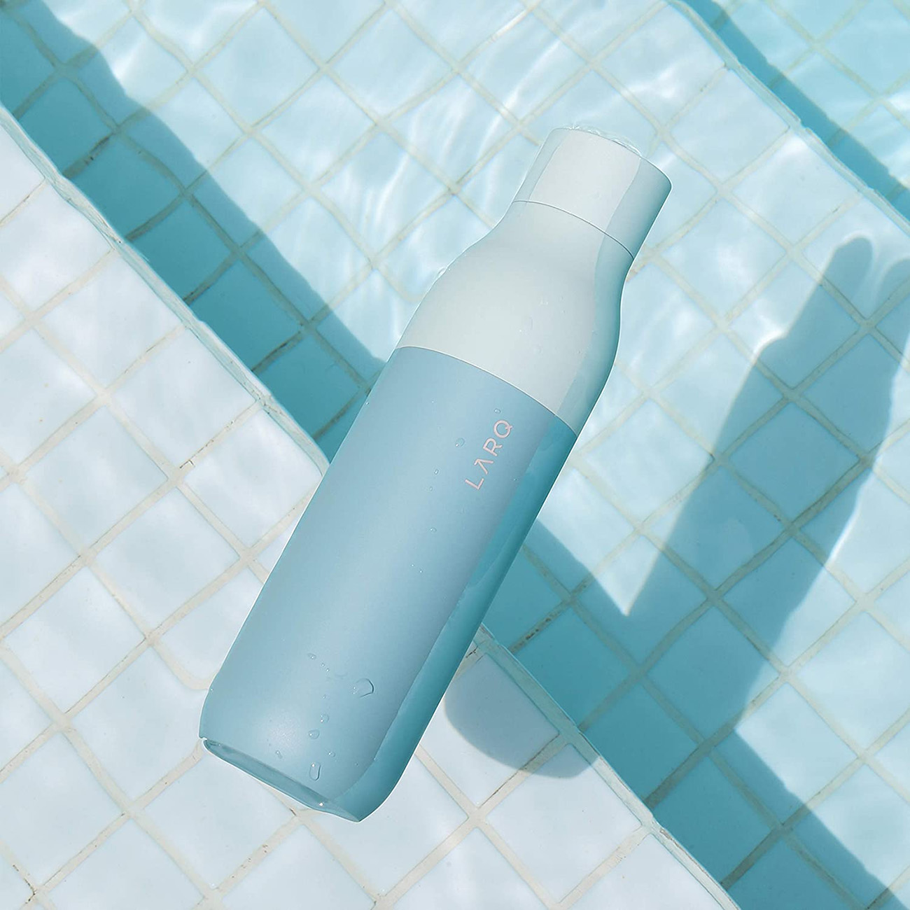 Eine blau-weiße Wasserflasche, die in blauem Wasser schwimmt. Das Wasser hat quadratische Fliesen.