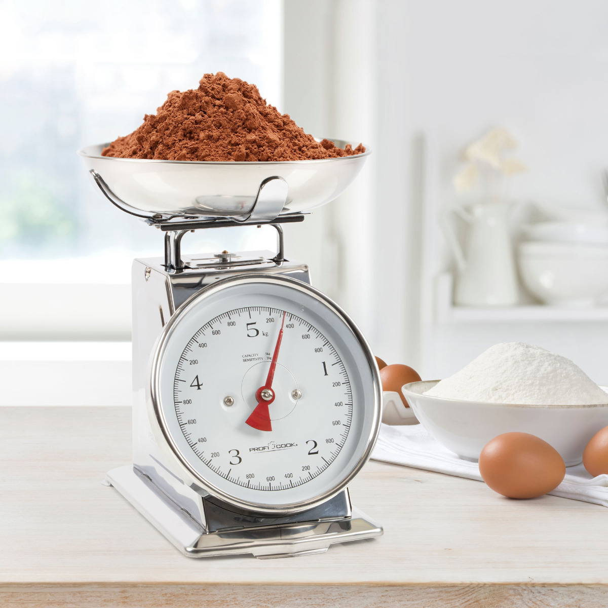 Waga kuchenna z miską z brązowym proszkiem; jajka i mąka w tle.