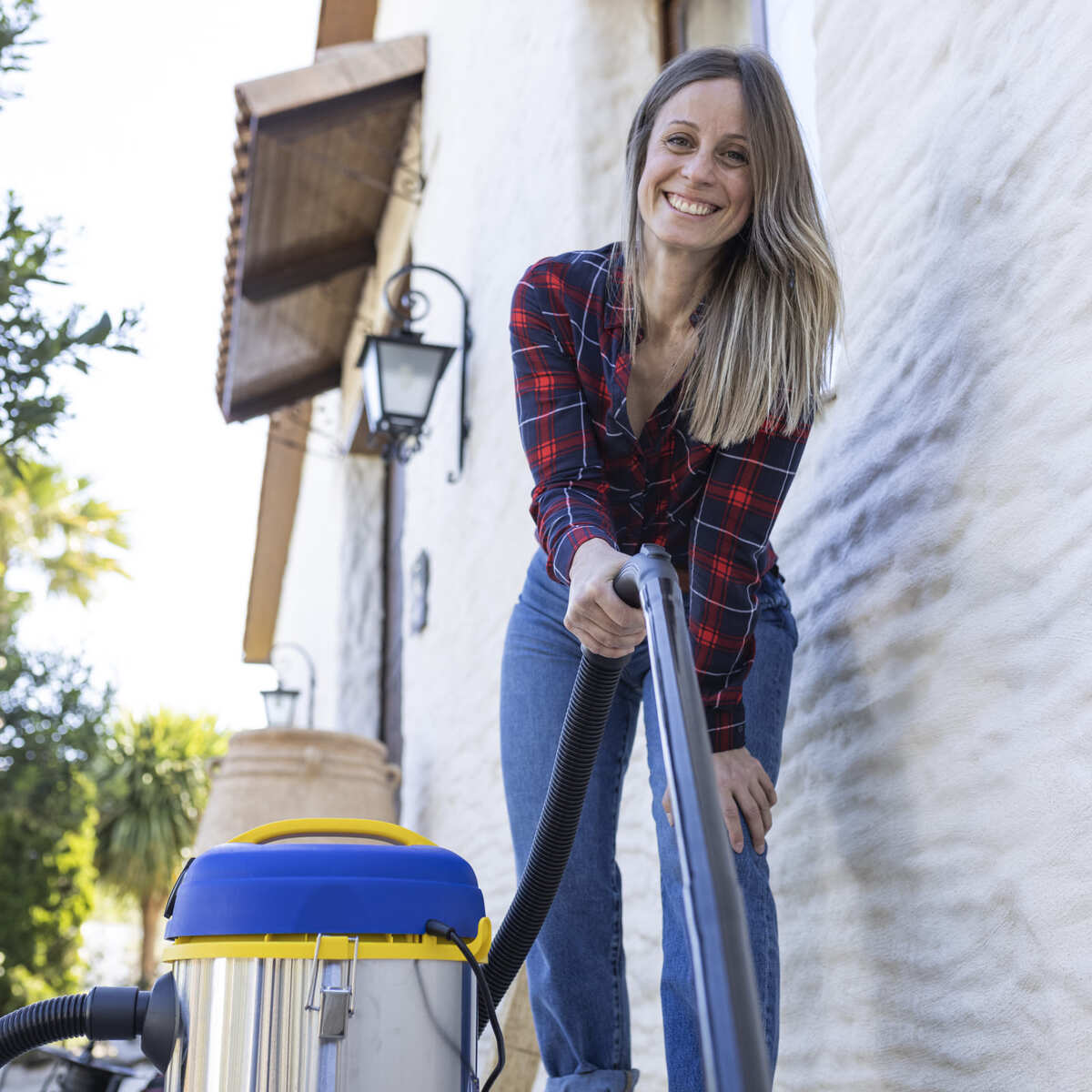 Una mujer aspirando un área al aire libre, sonriendo a la cámara.