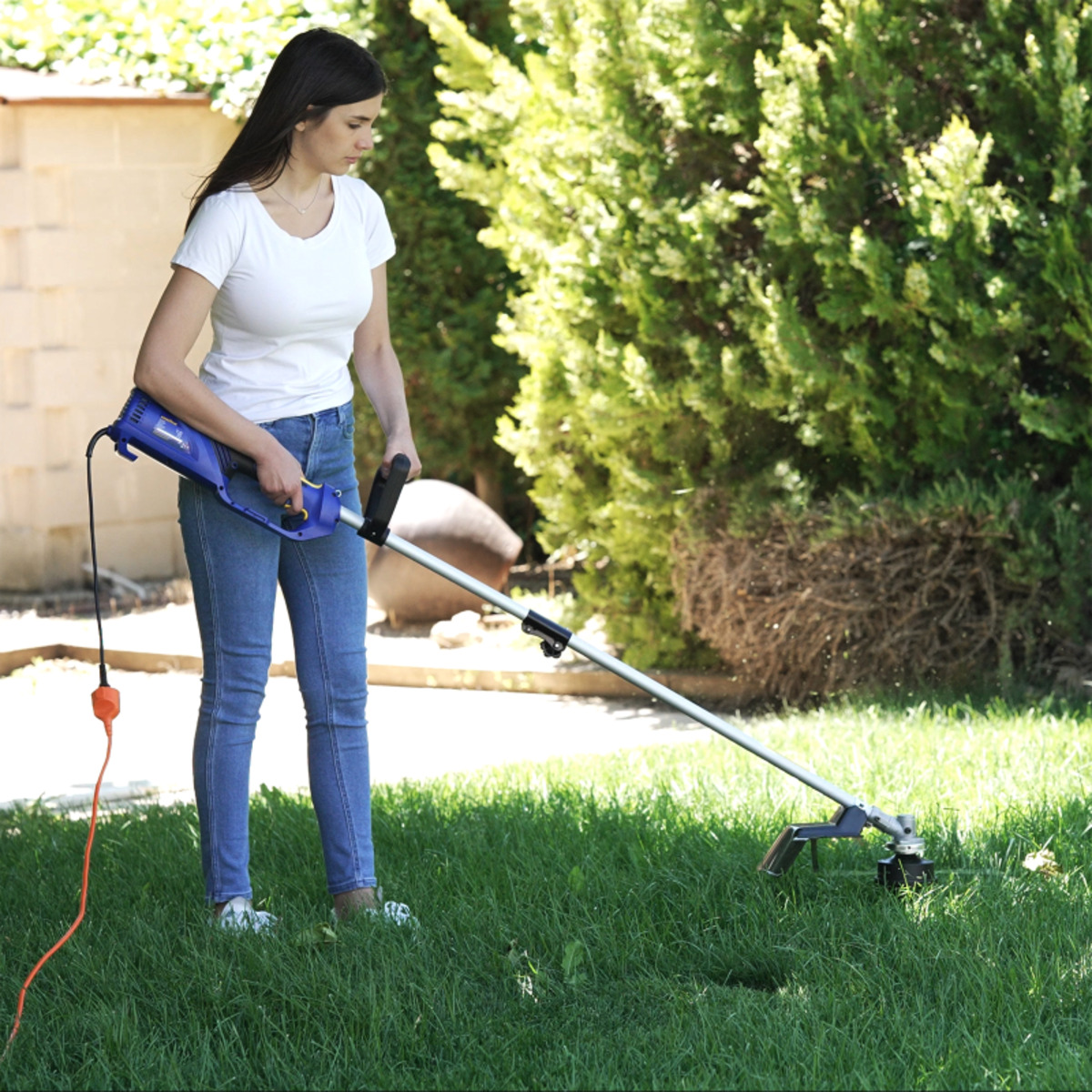 Mujer recortando hierba con un cortador eléctrico azul y negro en un jardín soleado.