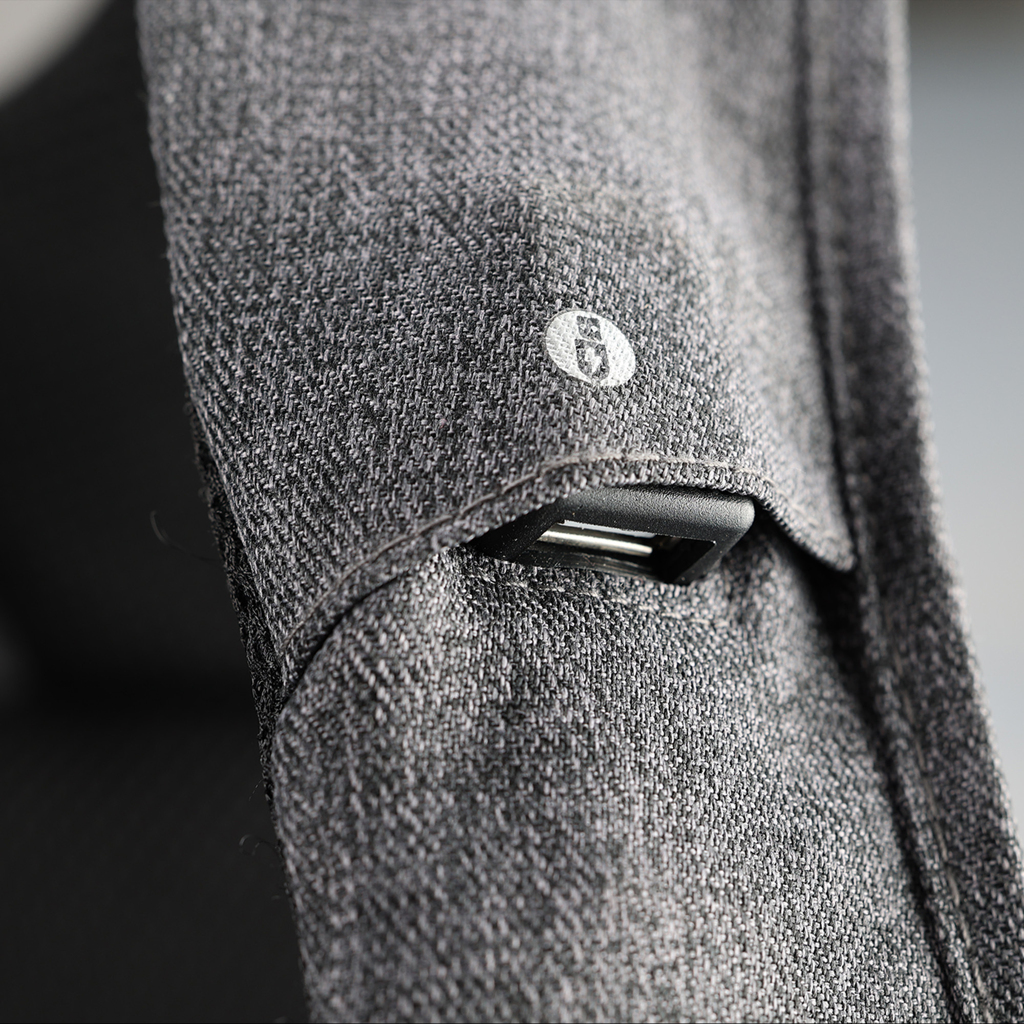 Primo piano di un tessuto grigio con una piccola copertura per porta USB nera e un bottone con logo bianco.
