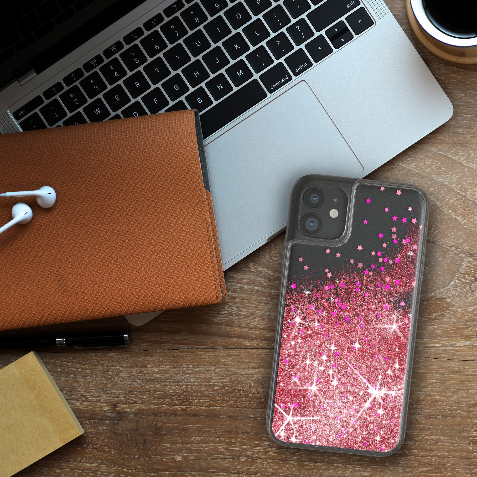 Ein Telefon mit einer pinkfarbenen Glitzerstern-Hülle liegt auf einem Holztisch. Ein Laptop und andere Gegenstände sind in der Nähe.