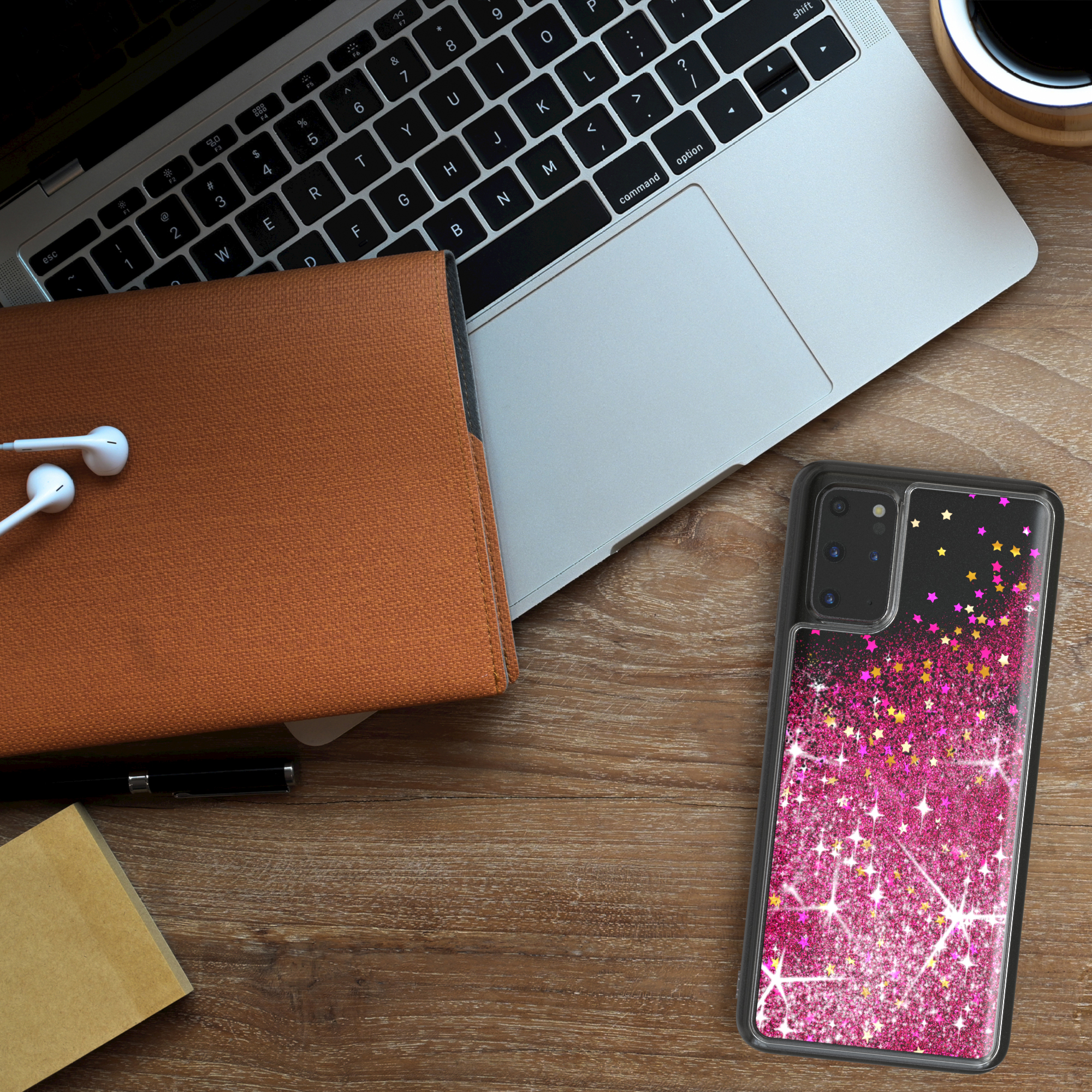 Ein Laptop, ein Telefon mit pinker Hülle, ein Notizbuch und Kopfhörer auf einem Holzschreibtisch.