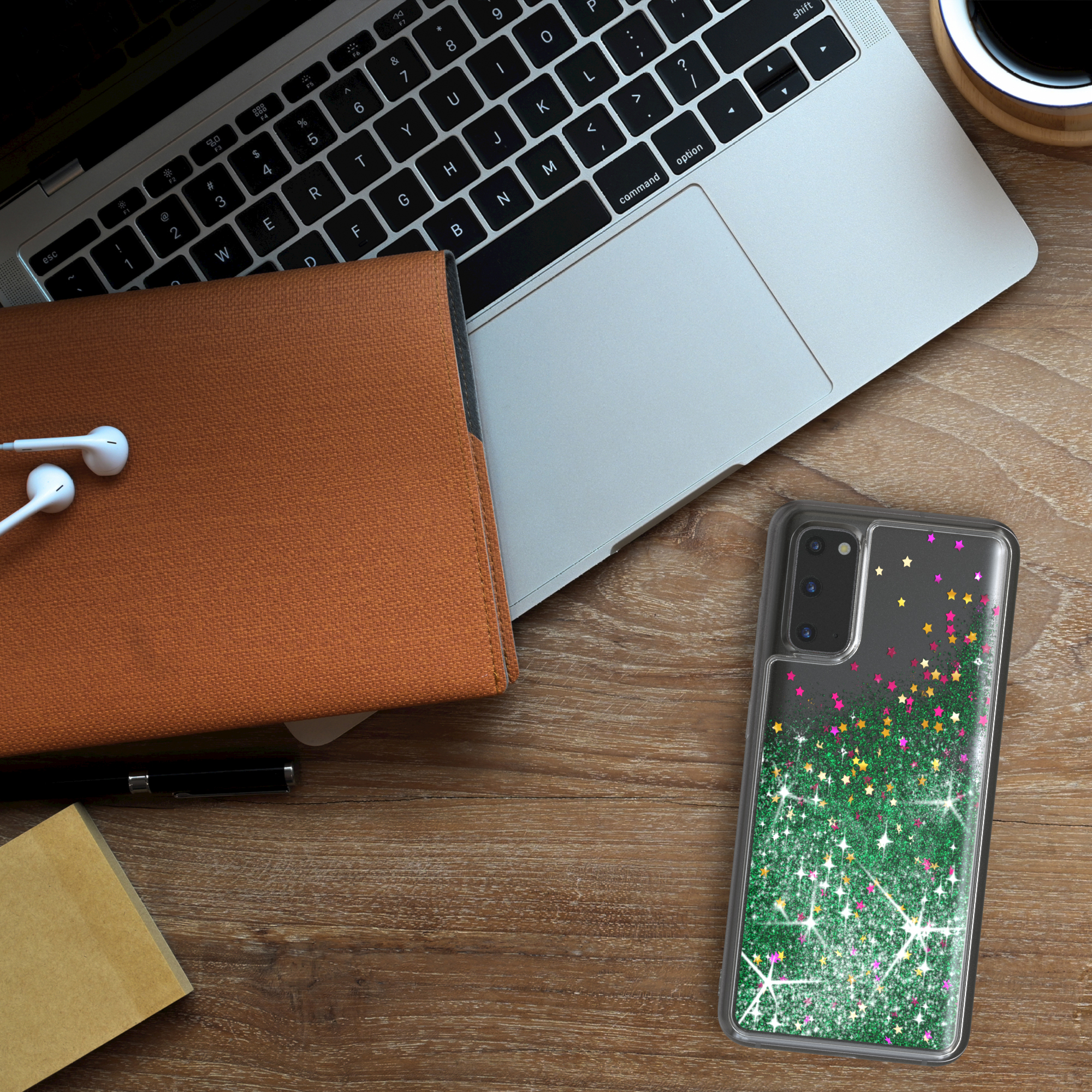 Eine Handyhülle mit glitzerndem grünen Design liegt auf einem Holzschreibtisch neben Laptop.