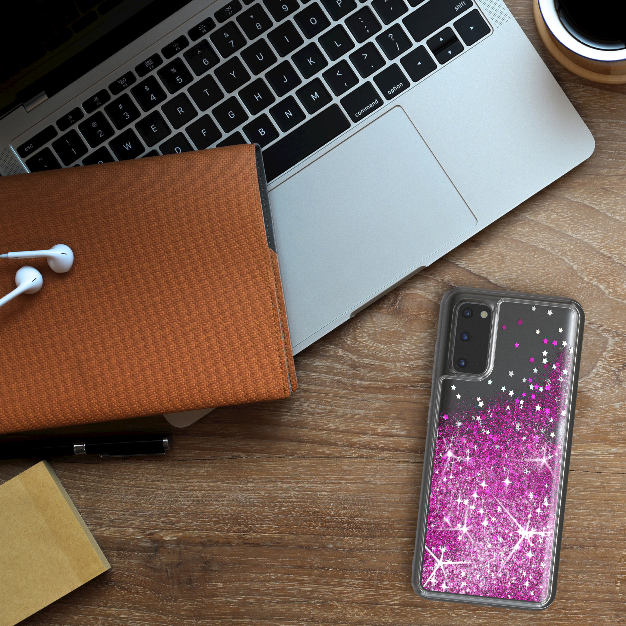 Laptop, Telefon mit pinker Glitzerhülle, Notizbuch, Stift und Ohrhörer auf einem Holzschreibtisch.