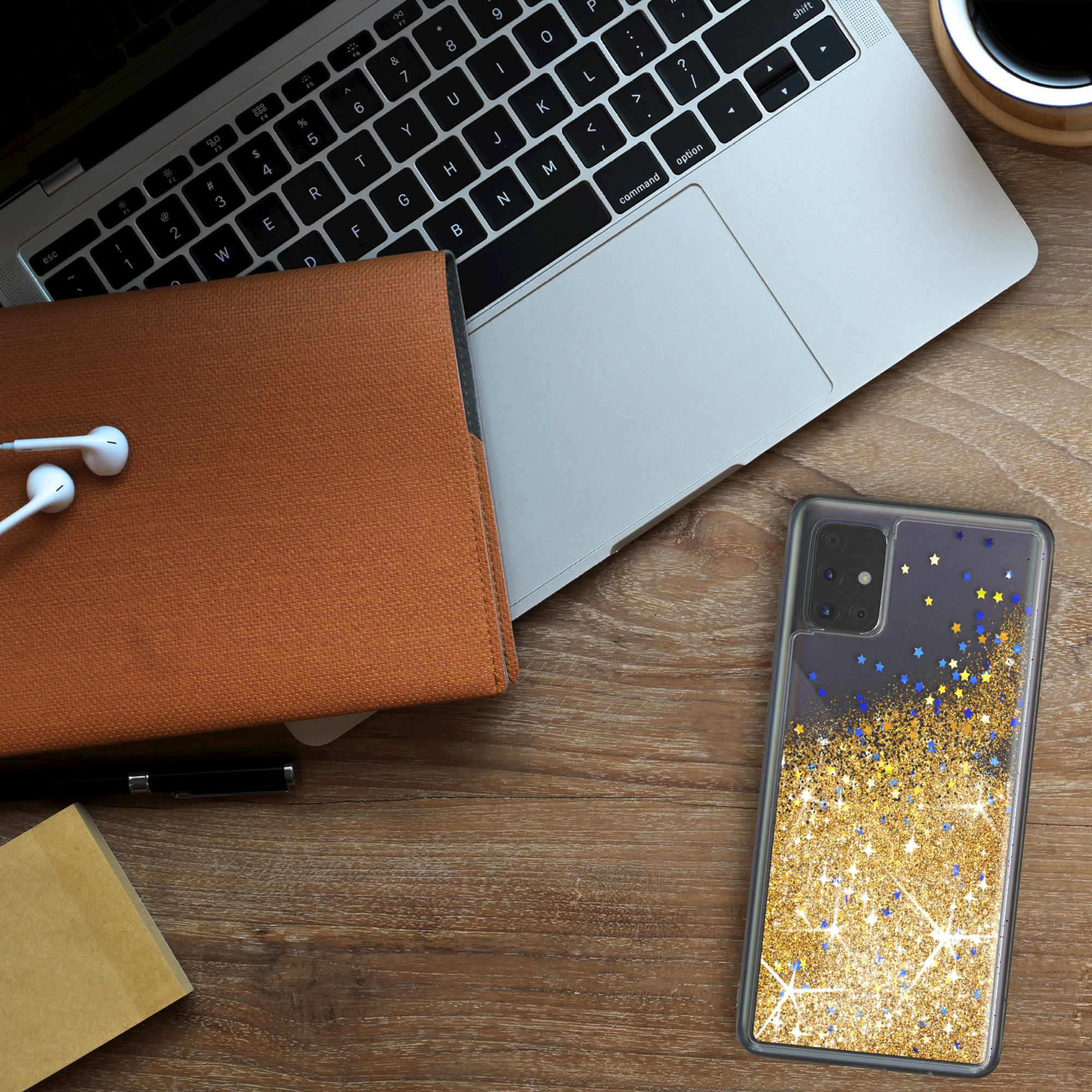Eine Handyhülle mit Gold- und Blauglitzer und ein Telefon auf einem Holzschreibtisch mit Gegenständen drumherum.