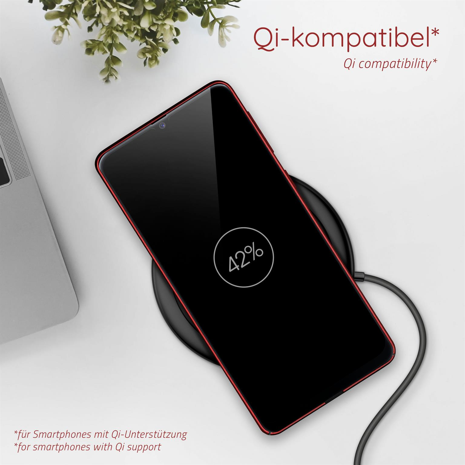 Telefon auf Ladegerät, 42% geladen. Weiße Oberfläche, Pflanze im Hintergrund.