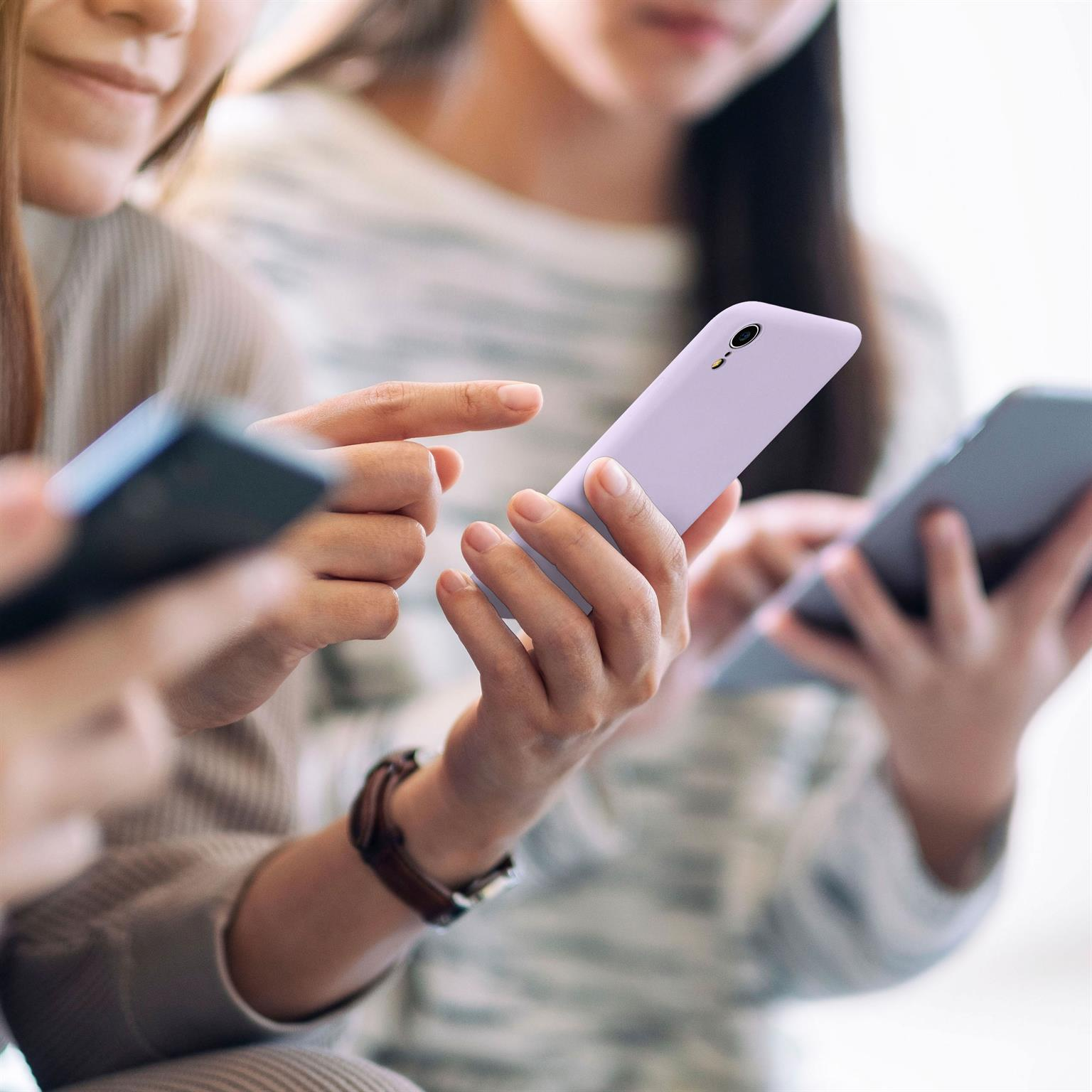 Drei Personen mit Handys. Einer hält ein lila Telefon. Verschwommener Hintergrund.