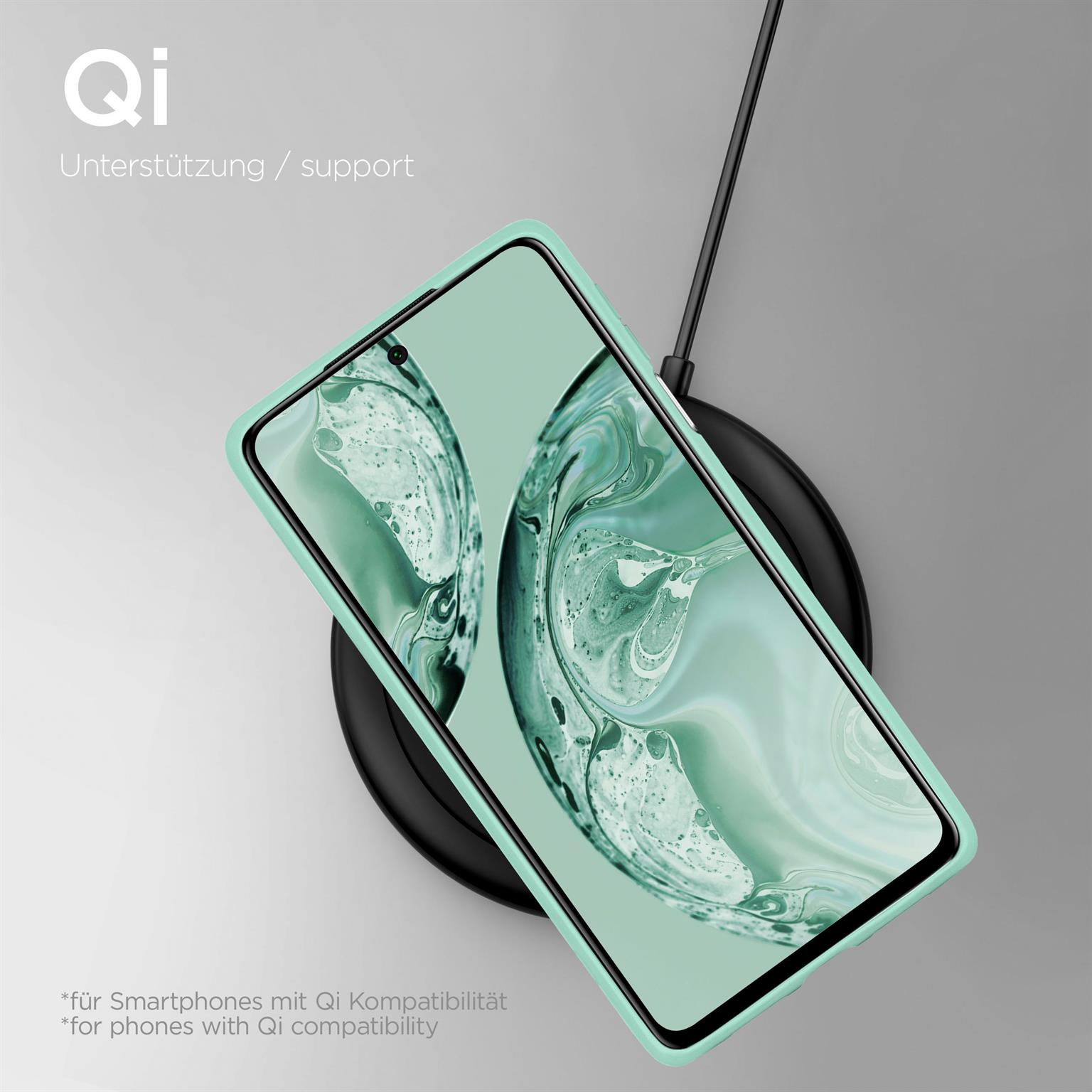 Telefon mit türkisfarbenem Gehäuse wird auf einem schwarzen kabellosen Ladegerät geladen. Weißer Hintergrund, Text.