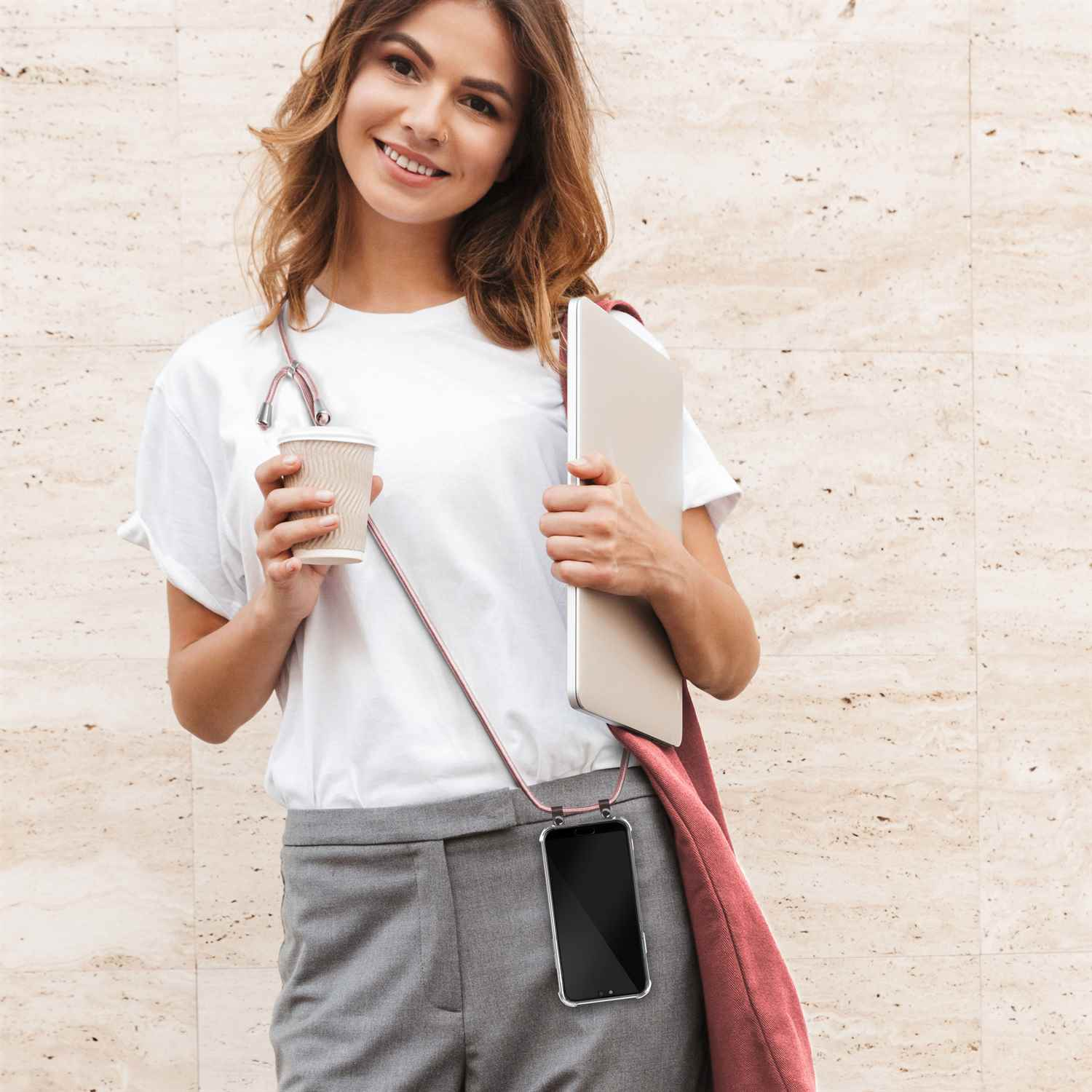 Frau, die eine Kaffeetasse und einen Laptop hält, mit einem Telefon, das mit einem Band am Hals befestigt ist.
