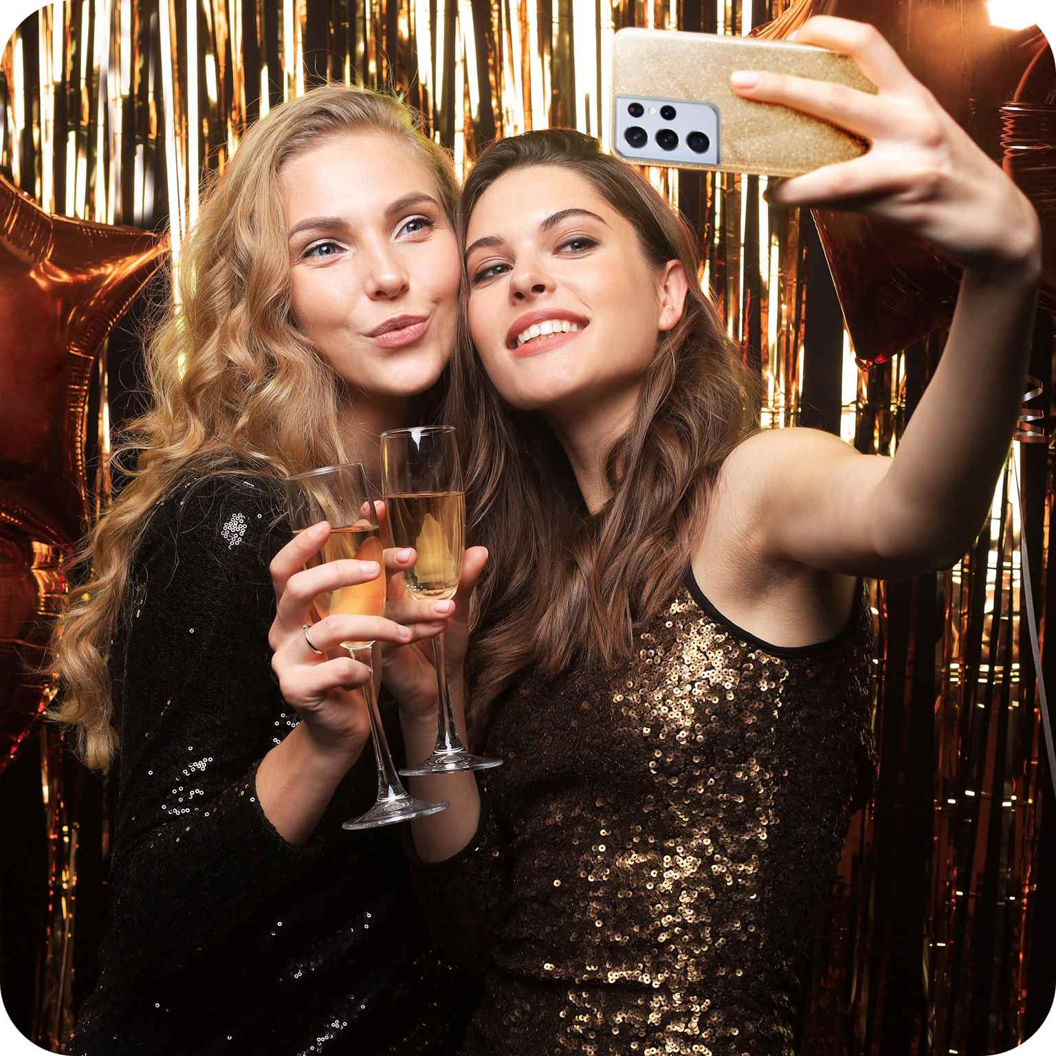 Zwei Frauen machen ein Selfie mit Champagnergläsern, mit goldenem Hintergrund.