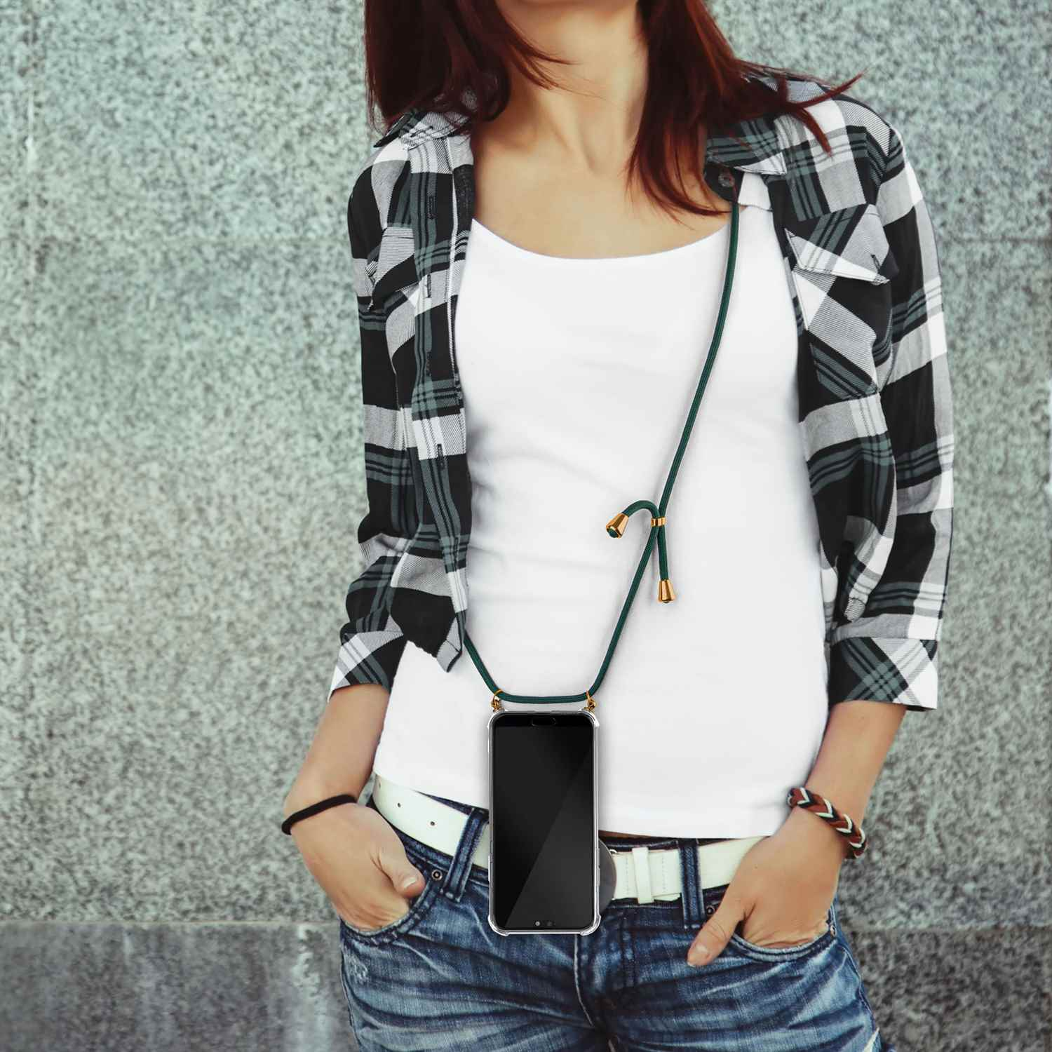 Frau mit schwarz-weiß kariertem Hemd, weißem Top, Jeans und grünem Telefon-Lanyard, die ein Telefon hält.