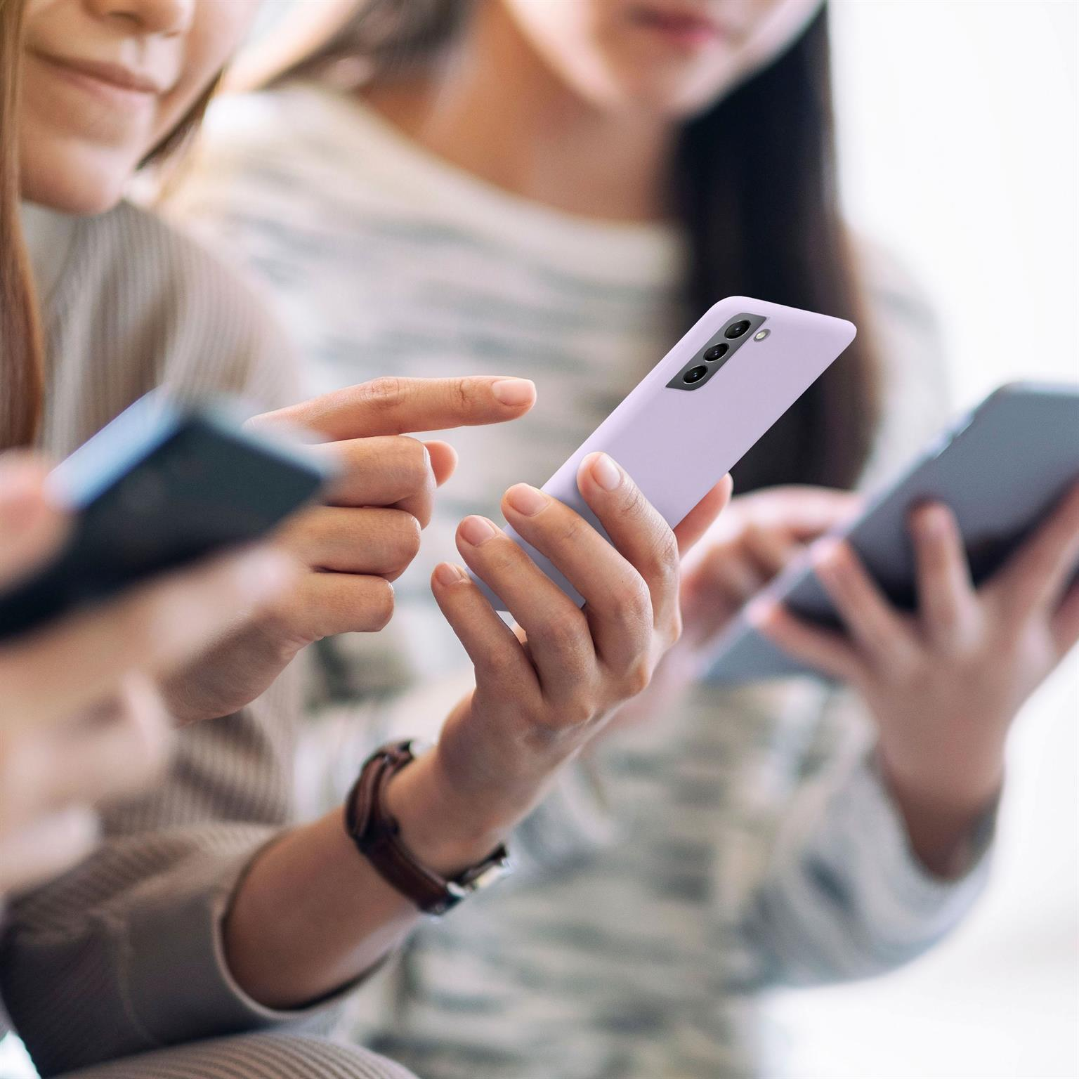Drei Personen benutzen Telefone, eines mit einer hellvioletten Hülle, in einer hellen Umgebung.