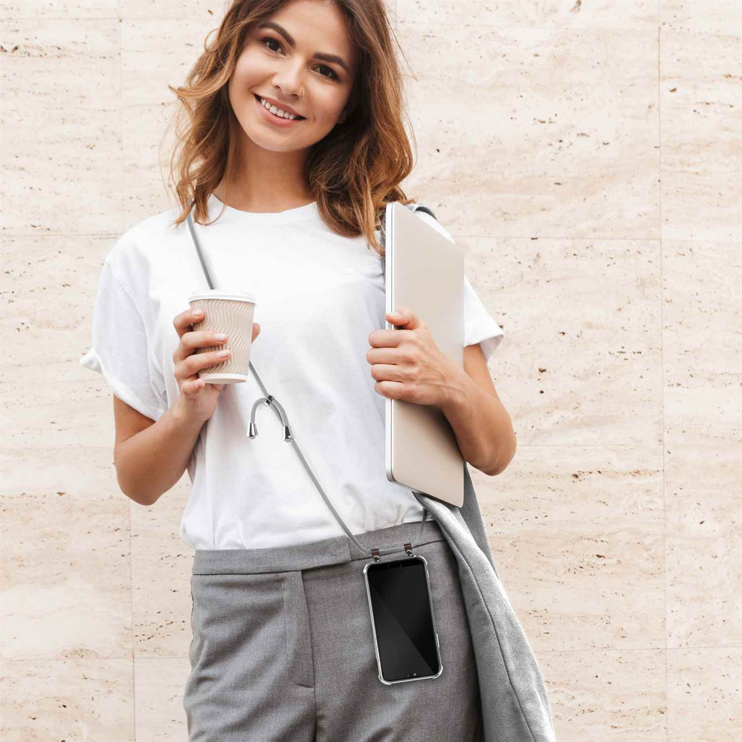 Eine Frau hält eine Tasse und einen Laptop, mit einem Telefon, das in einer durchsichtigen Hülle um ihren Hals hängt.