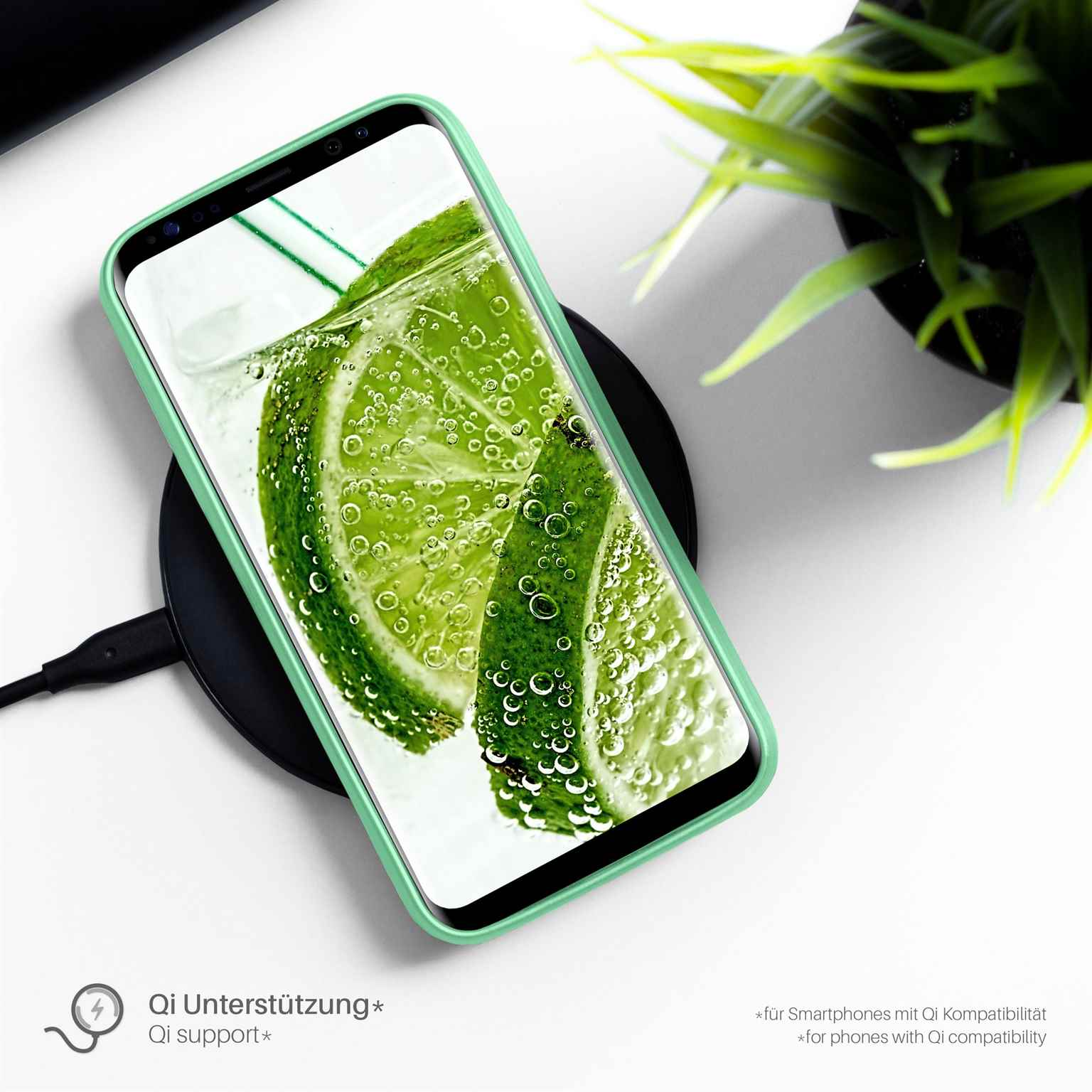 Telefon in grüner Hülle auf kabellosem Ladegerät mit Limettenscheiben in Wasser.