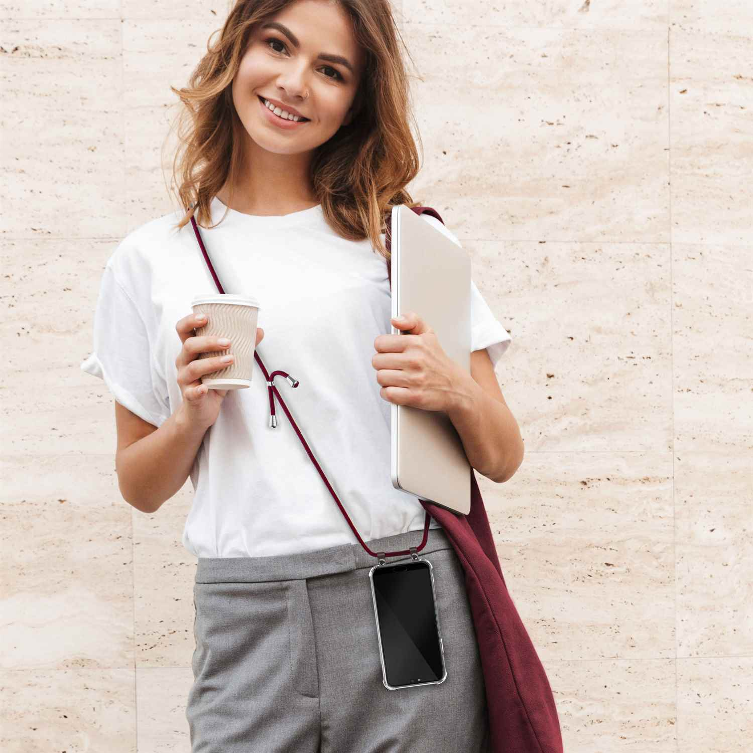 Frau hält Kaffee und Laptop, trägt eine rote Handykordel.