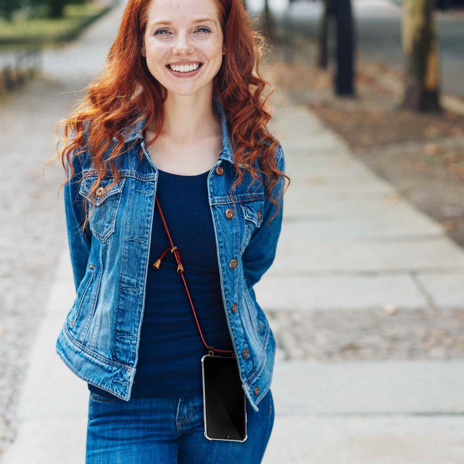 Frau mit roten Haaren trägt Jeansjacke und Jeans, hält Telefon mit Kordel.