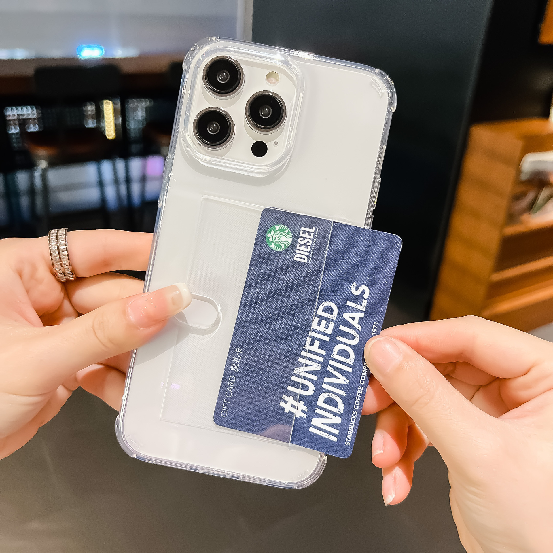 Hände halten ein Telefon in einer durchsichtigen Hülle mit einer Starbucks-Geschenkkarte im Kartenhalter.