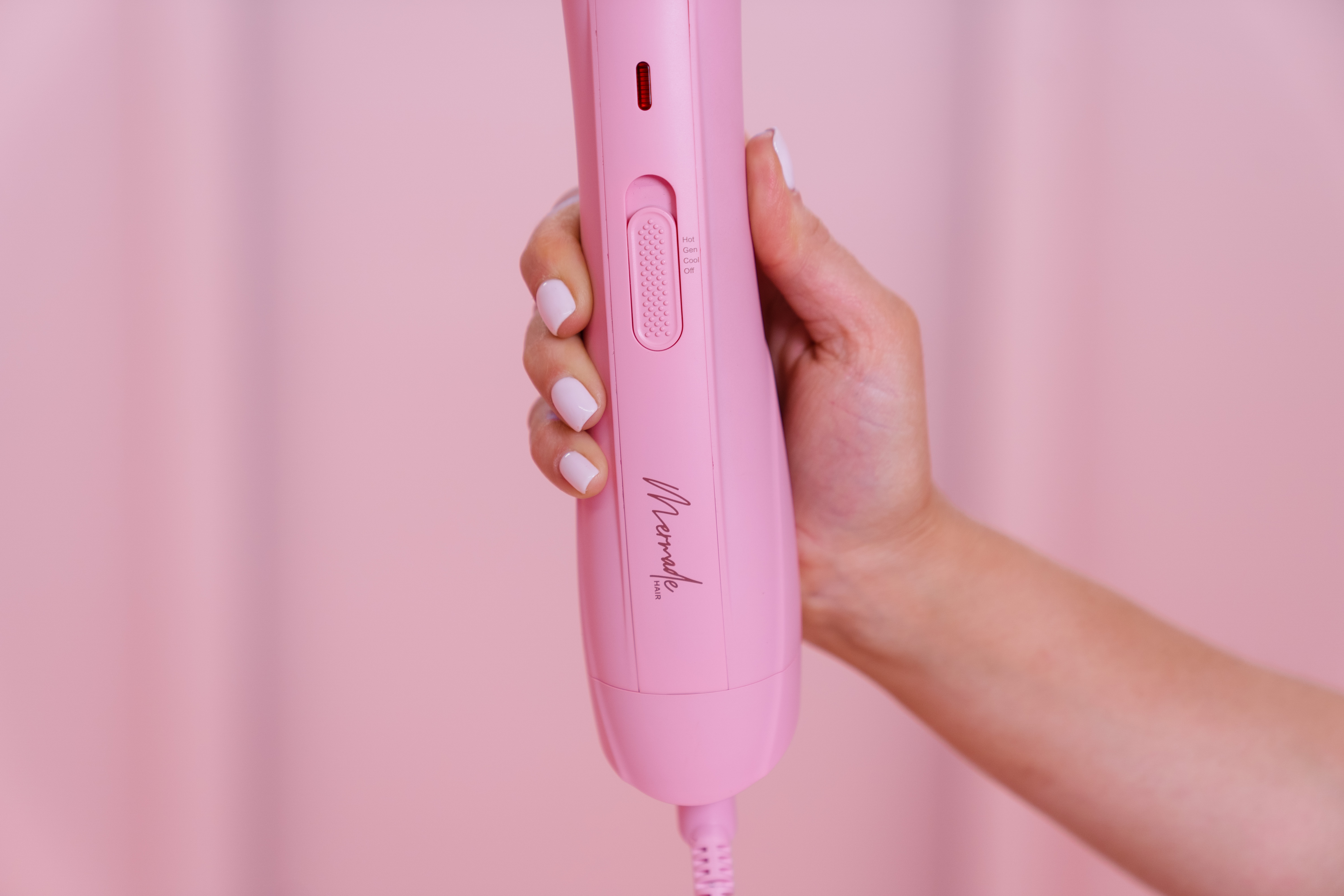 Eine Hand, die ein rosa Haarstyling-Gerät mit rosa Hintergrund hält.