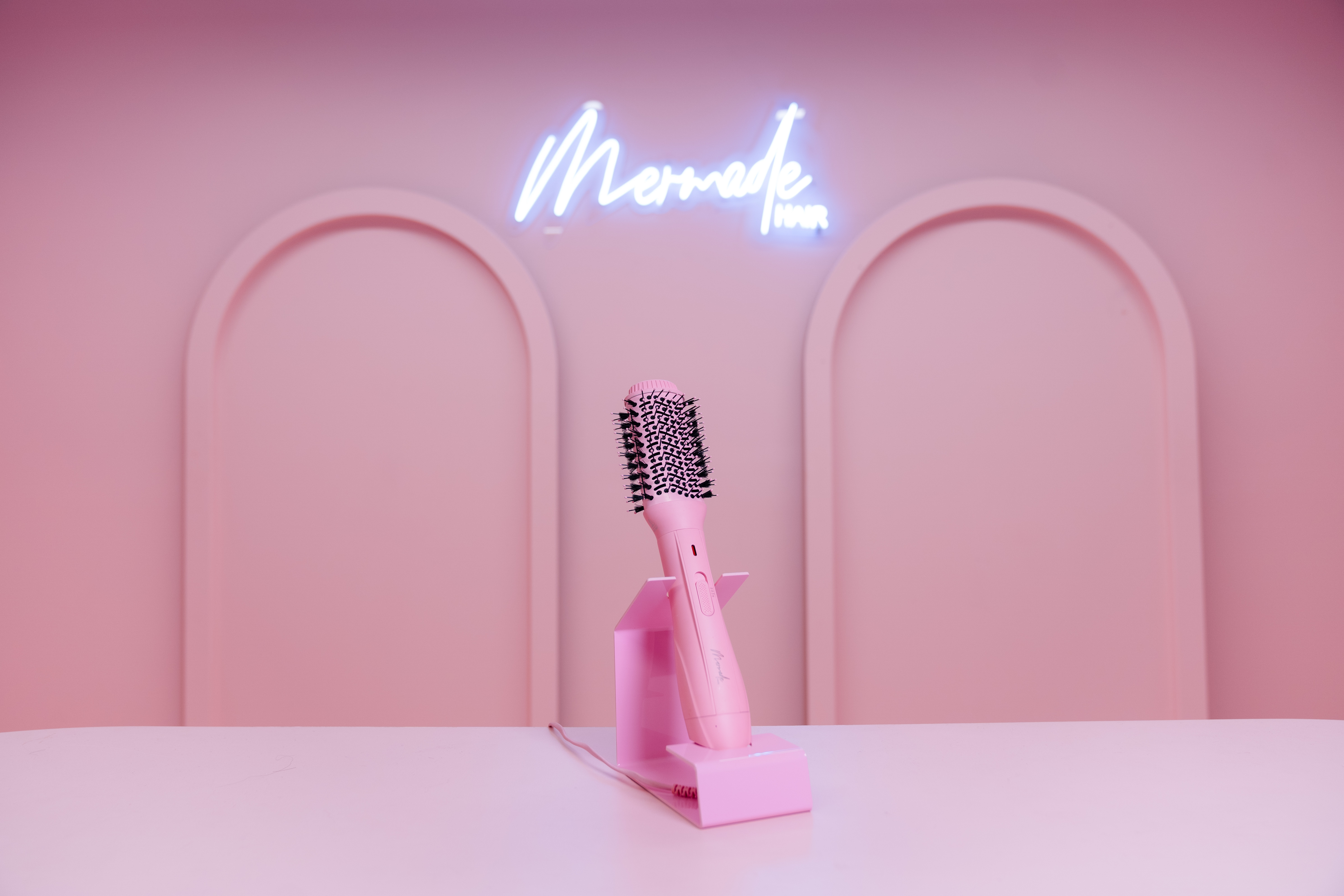 Eine rosa Haarstylingbürste in einem rosa Raum mit dem Neonschild „Mermade Hair“ darüber.