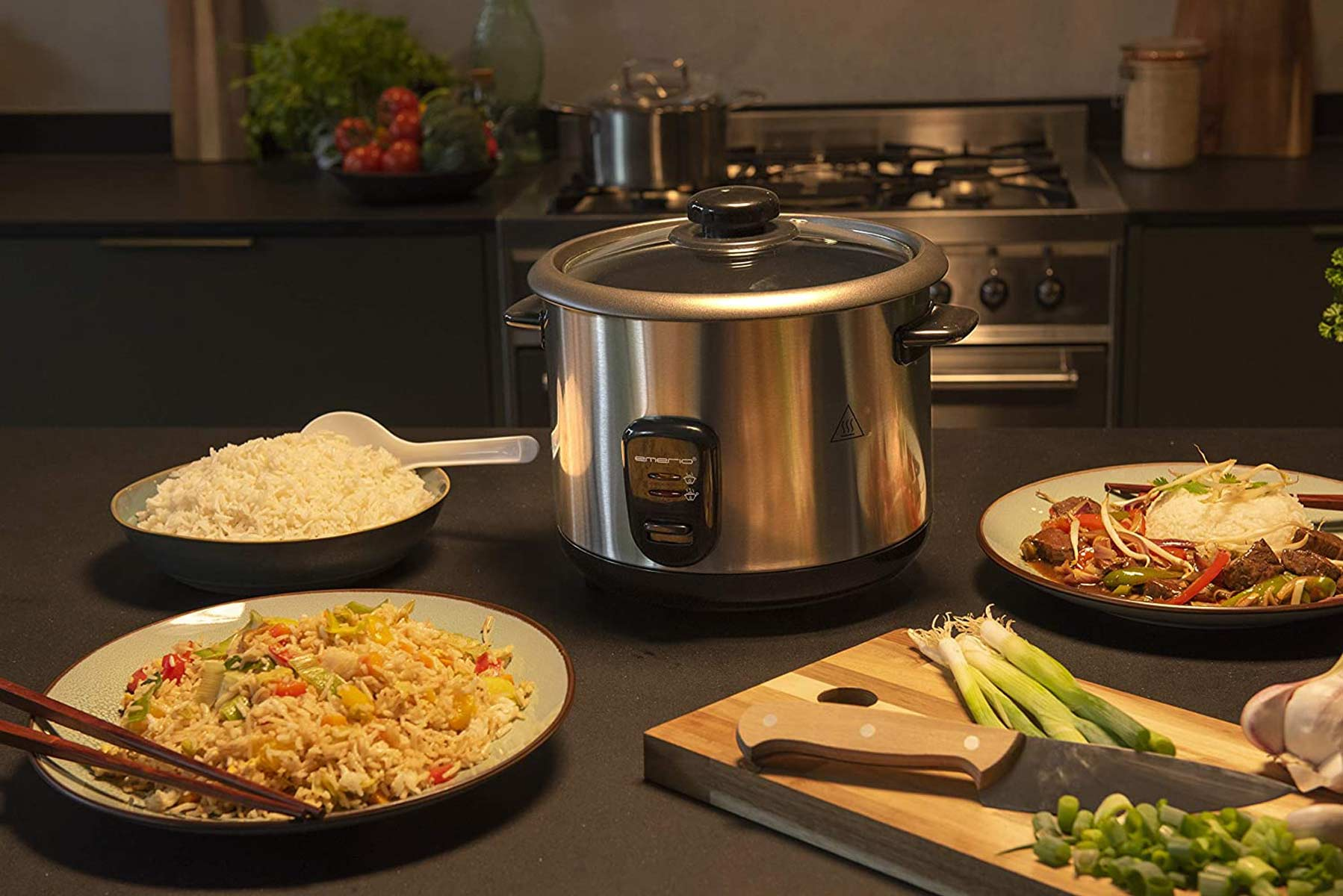 Arrocera, arroz cocido, arroz frito e ingredientes sobre una mesa en la cocina.