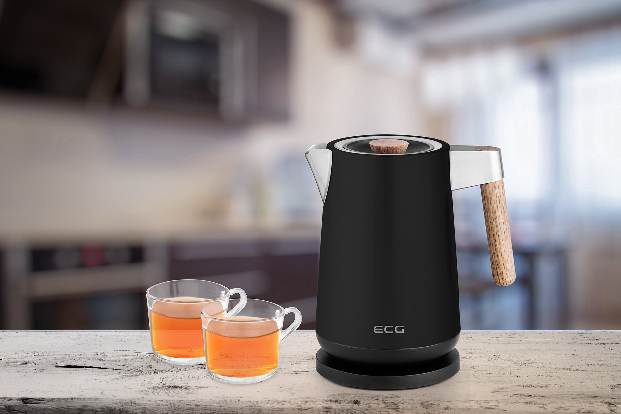 Czarny czajnik elektryczny z drewnianym uchwytem i dwie filiżanki herbaty na drewnianym stole z rozmytym tłem.