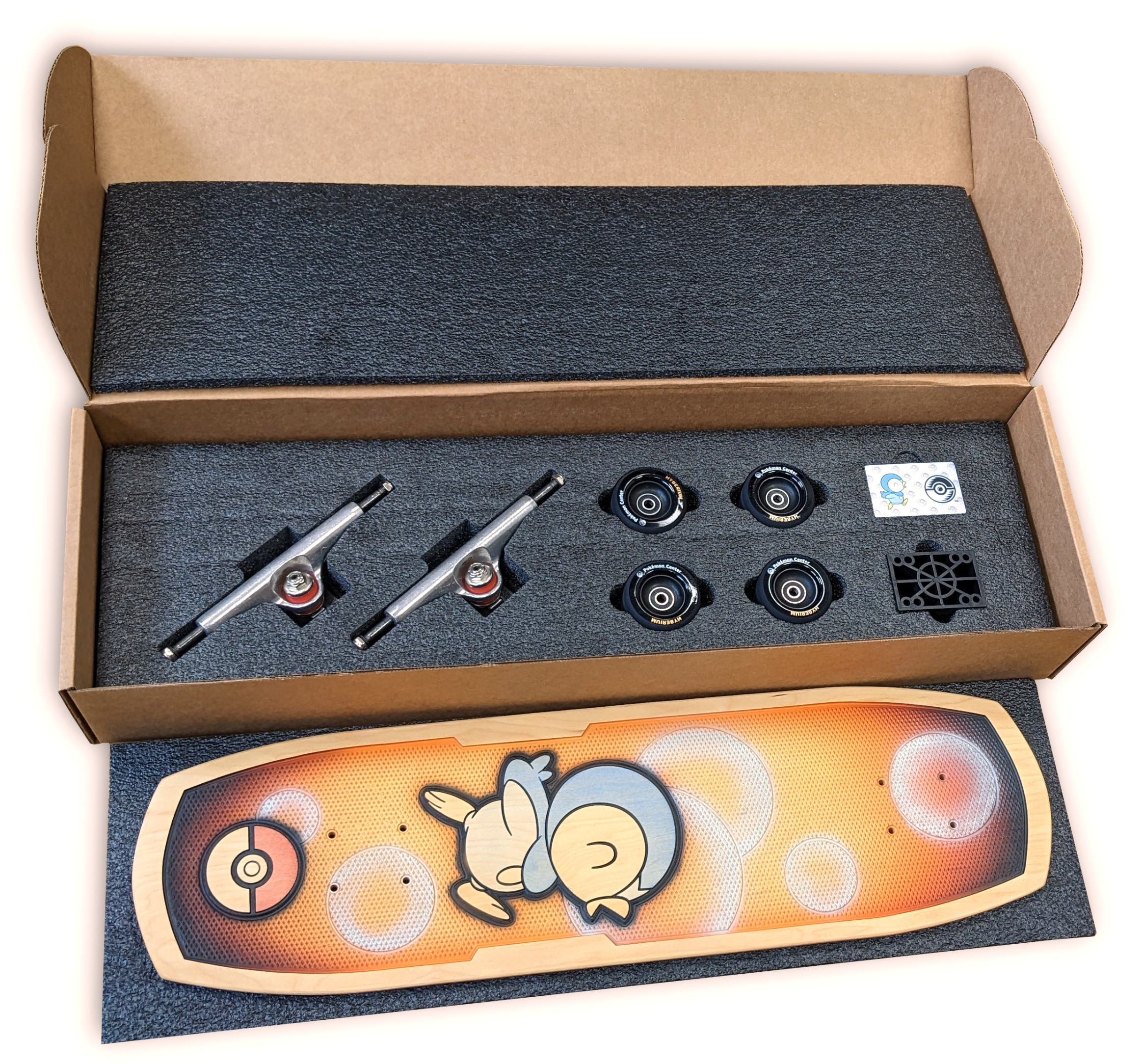 Skateboard-Teile in einer Box, darunter Achsen, Rollen und ein Deck mit einer Cartoonfigur.