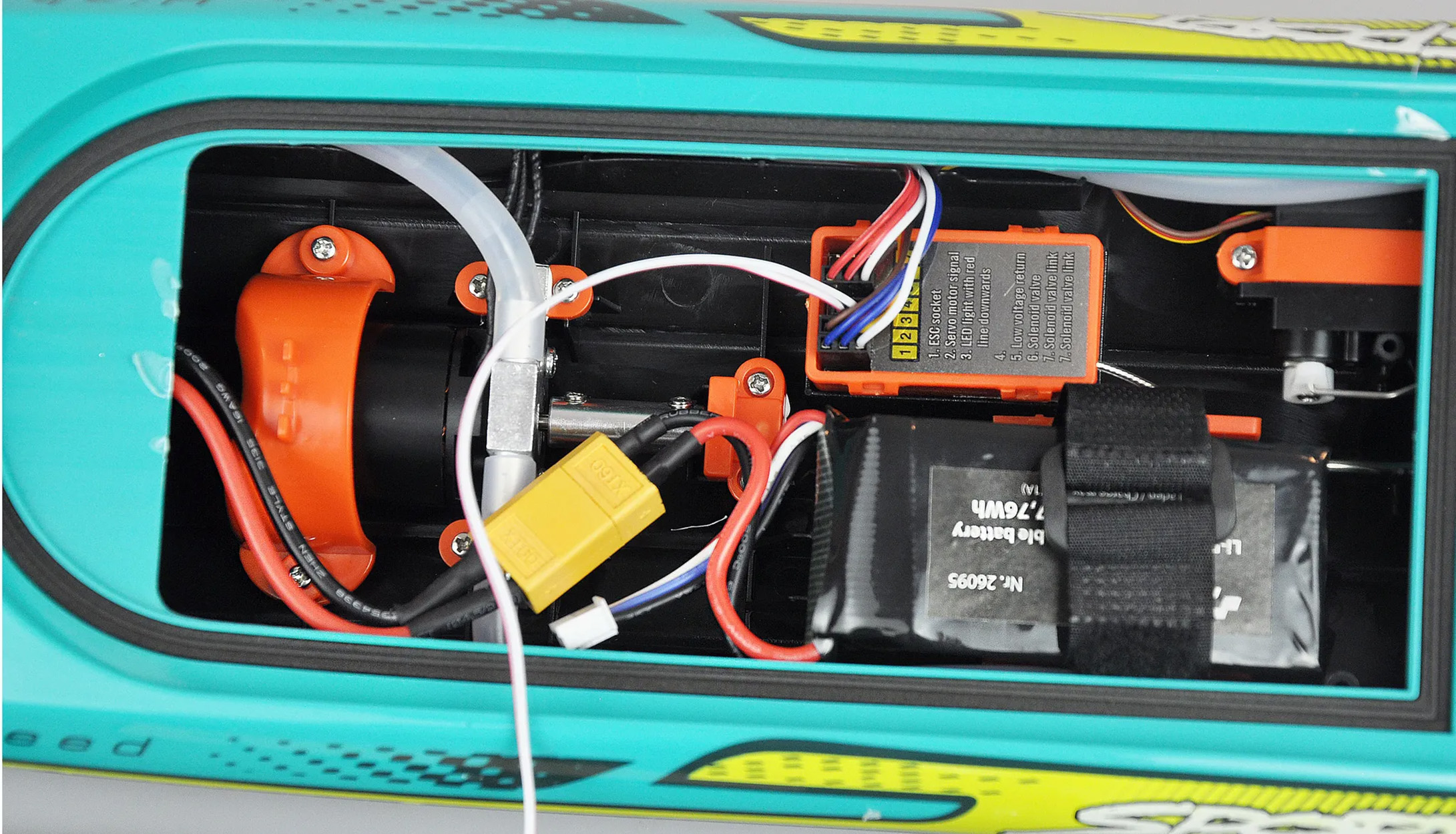 Innenansicht eines Modellbootes mit elektrischen Bauteilen, Drähten und einer Batterie.