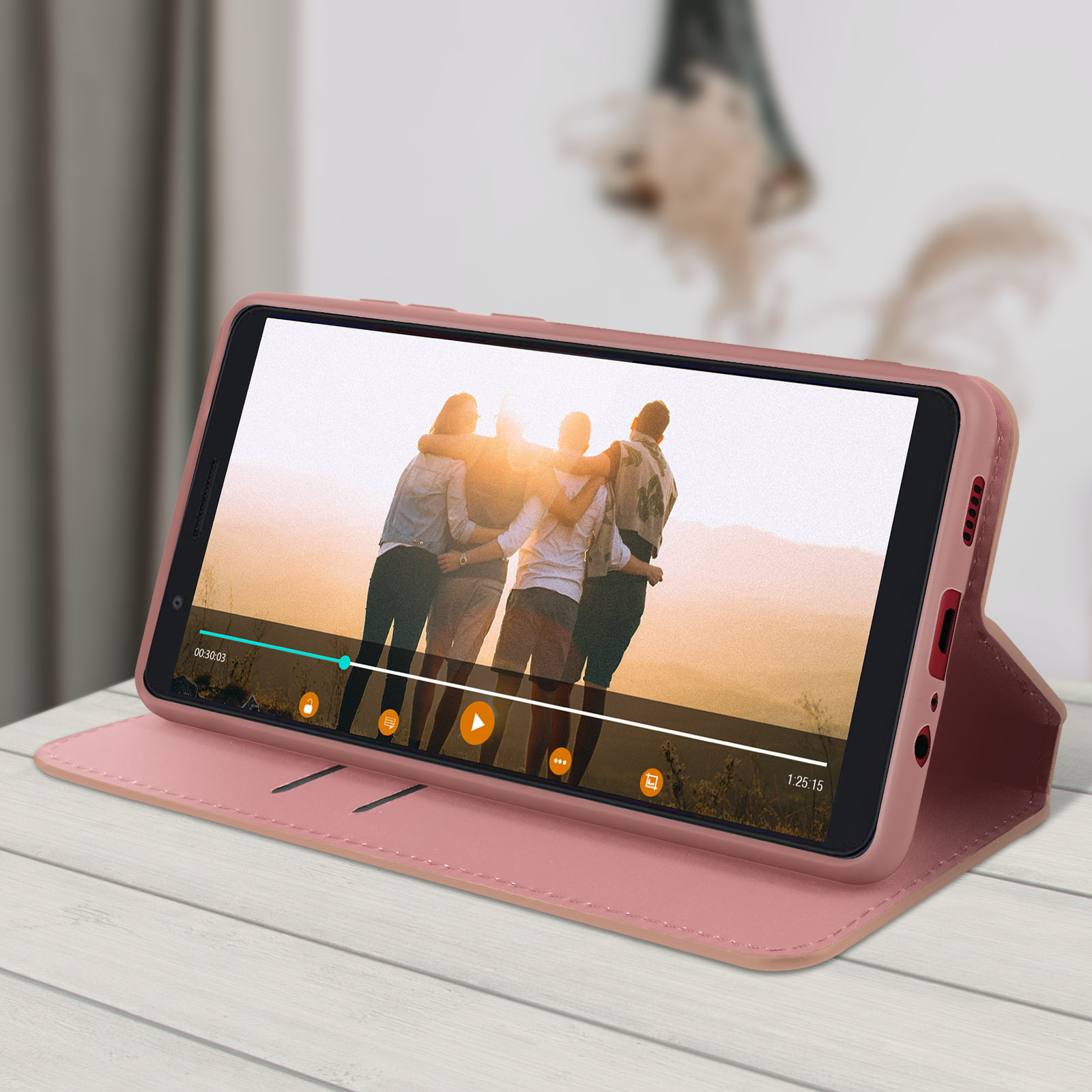 Un téléphone dans un étui rose affiche une vidéo de personnes s'embrassant. Le téléphone est sur une table en bois blanc.