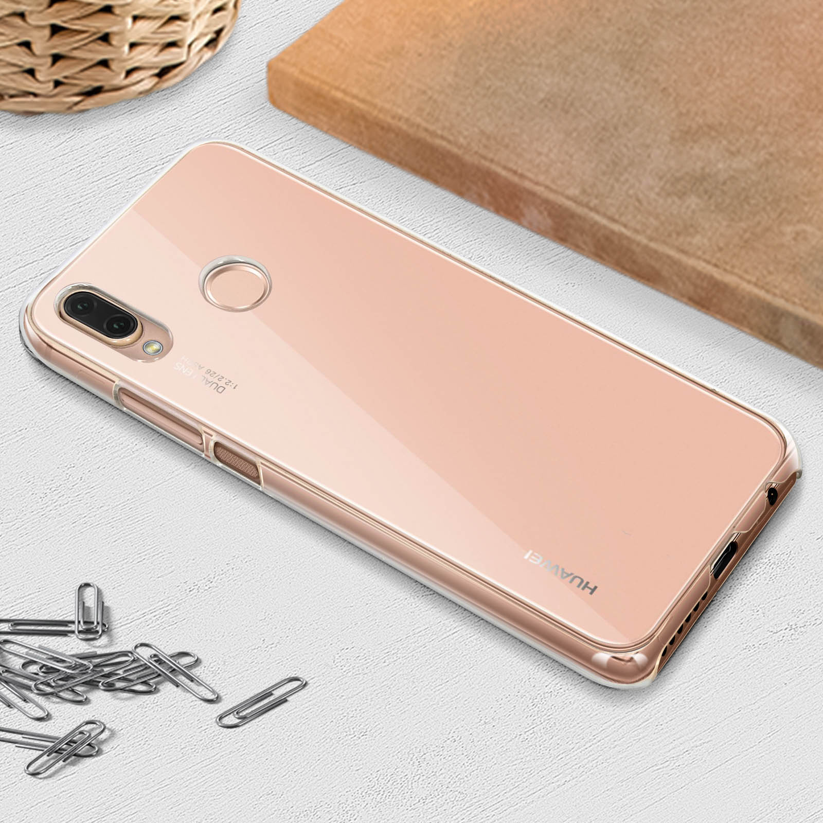 Telefono oro rosa con custodia trasparente su superficie di legno, circondato da oggetti.