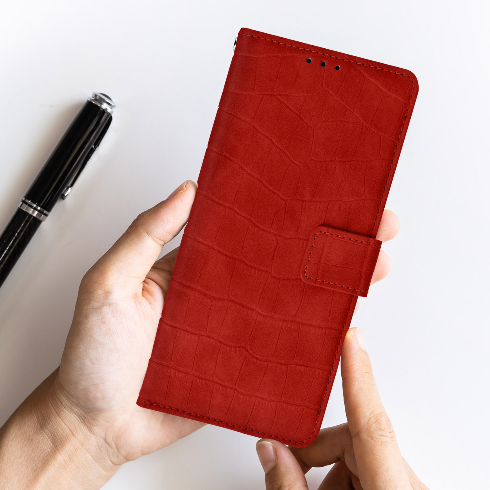 Custodia per telefono rossa con un design strutturato. Una mano tiene la custodia con una penna e sfondo bianco.