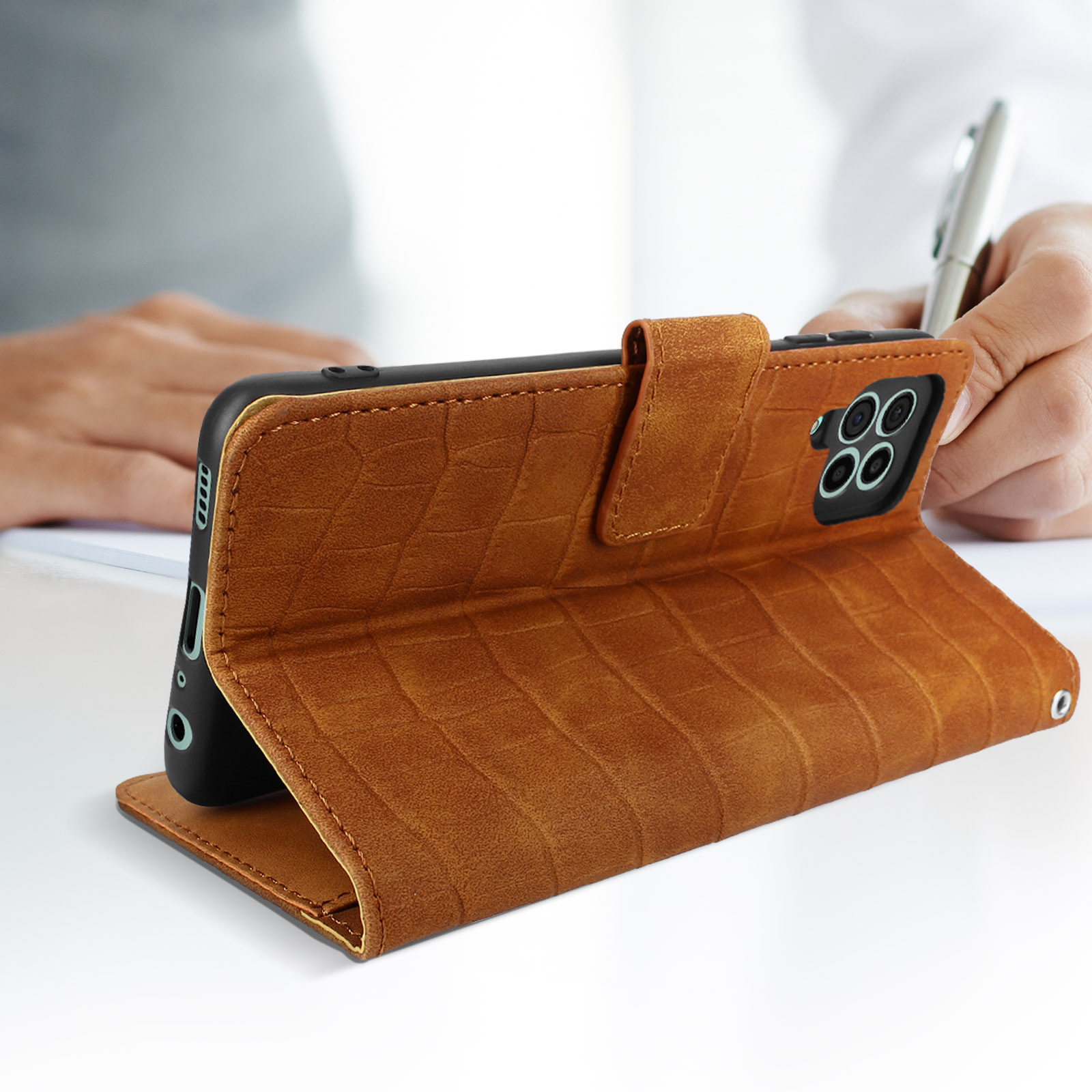 Funda de teléfono marrón con un teléfono dentro, apoyada para su visualización. La mano de una persona es visible.