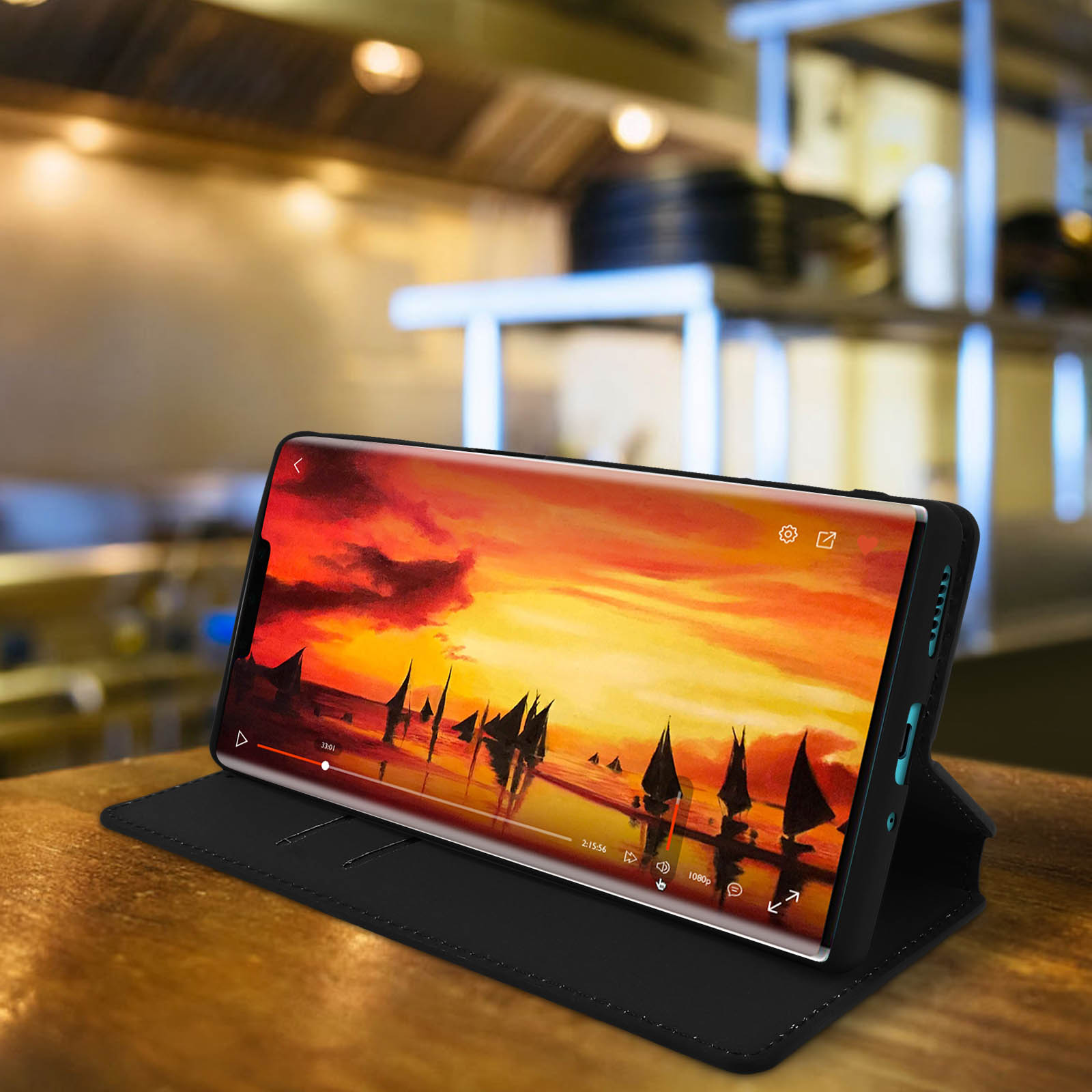 Telefono che mostra una scena di tramonto in una custodia nera, su una superficie di legno.