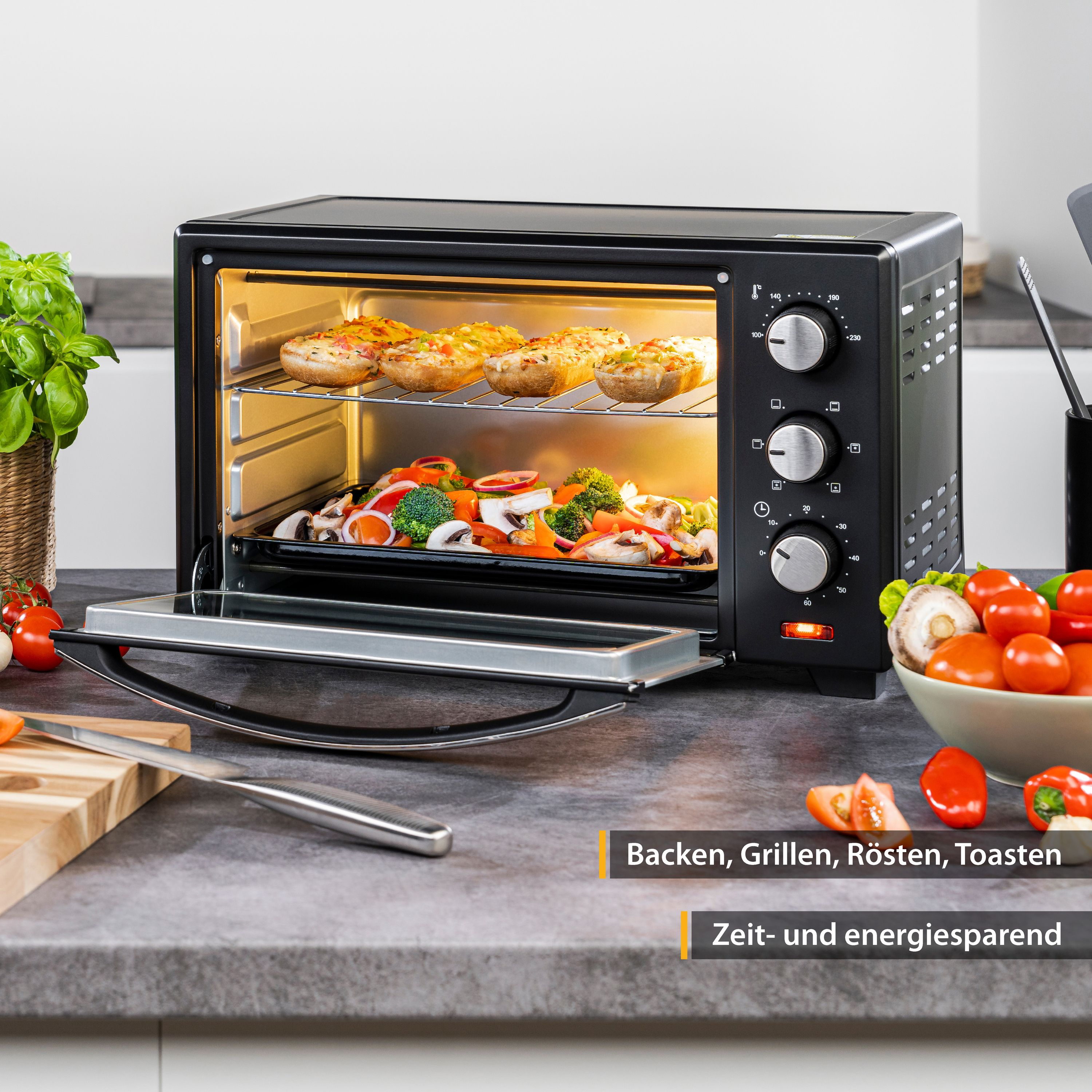 Schwarzer Ofen mit Essen, Tomaten und Gemüse. Text: Backen, Grillen, Toasten, Zeit sparen.