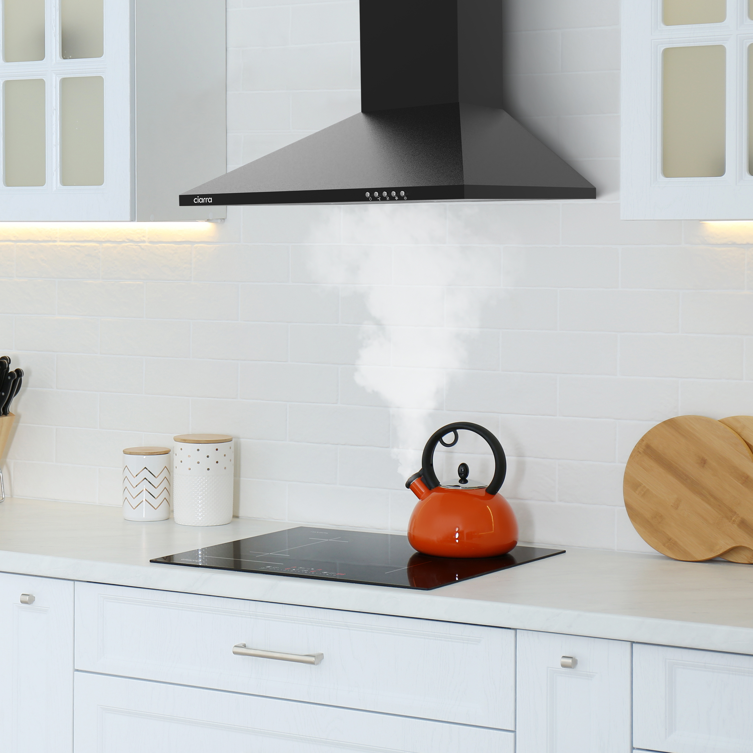 Keuken met afzuigkap. Oranje waterkoker op inductiekookplaat. Witte kasten.