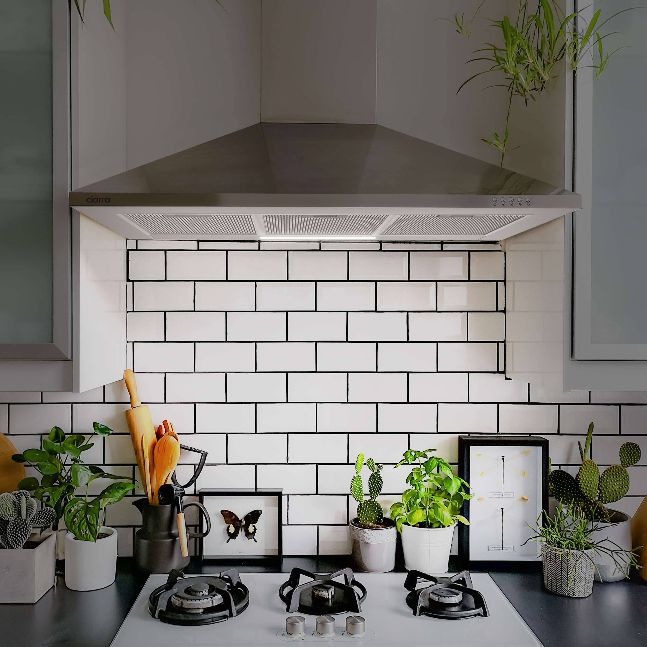 RVS afzuigkap boven witte tegel backsplash en kookplaat.
