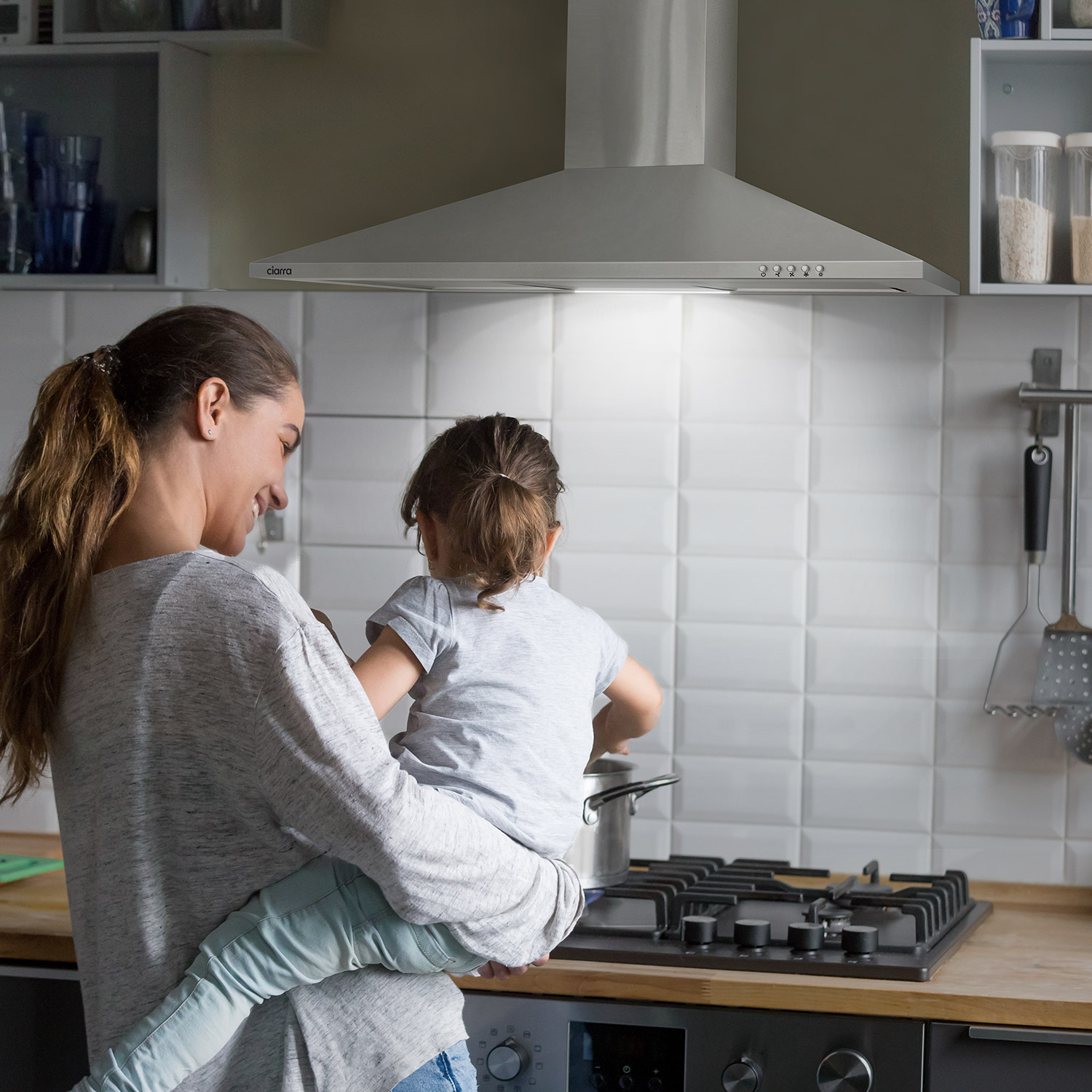 Vrouw met kind aan het koken in keuken, met roestvrijstalen afzuigkap.