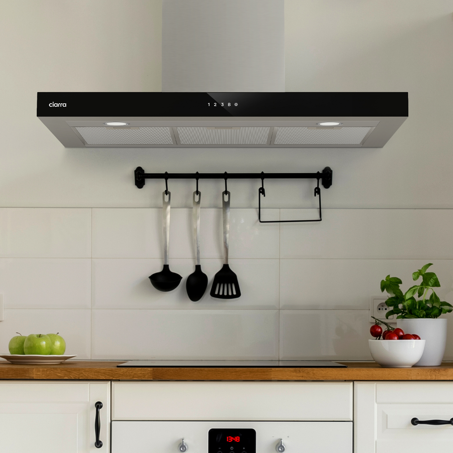 Una cappa nera sopra un mobile da cucina bianco, con utensili appesi.